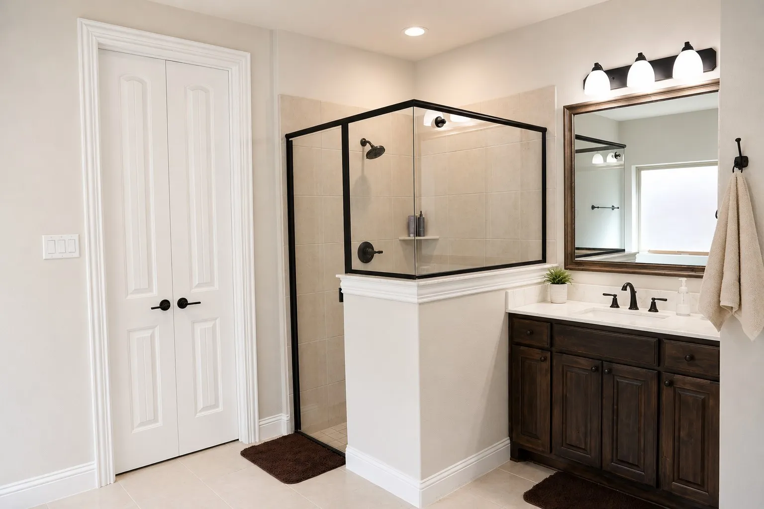 Spacious bathroom featuring a glass-enclosed shower with matte black hardware, a dark wood-finish vanity with a light-toned countertop, and a large framed mirror with integrated lighting