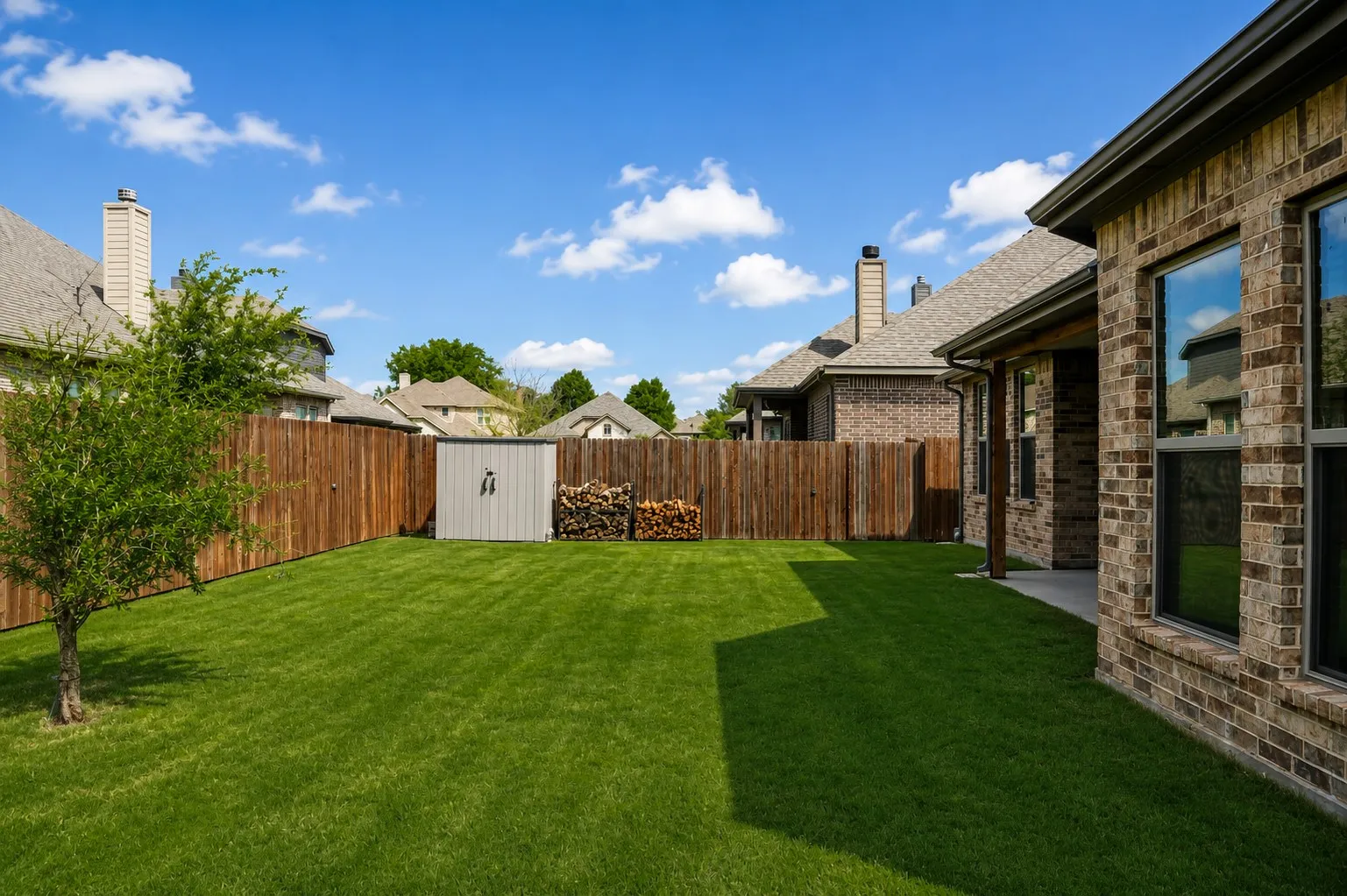 Expansive backyard featuring a manicured lawn, full privacy fencing, and a dedicated storage shed