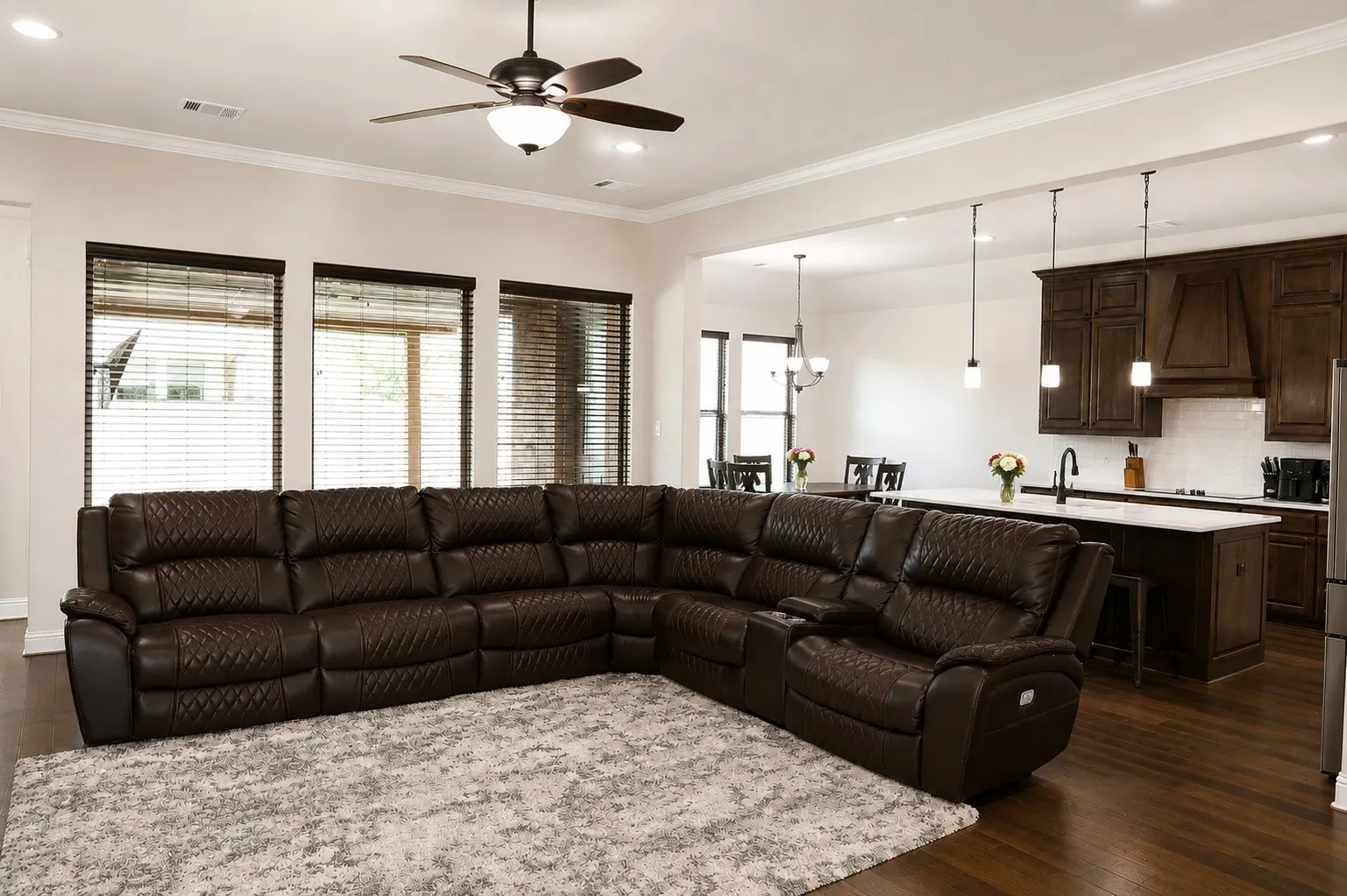 Open-concept living area featuring rich wood-finish flooring, a contemporary ceiling fan with integrated lighting, and multiple windows with blinds