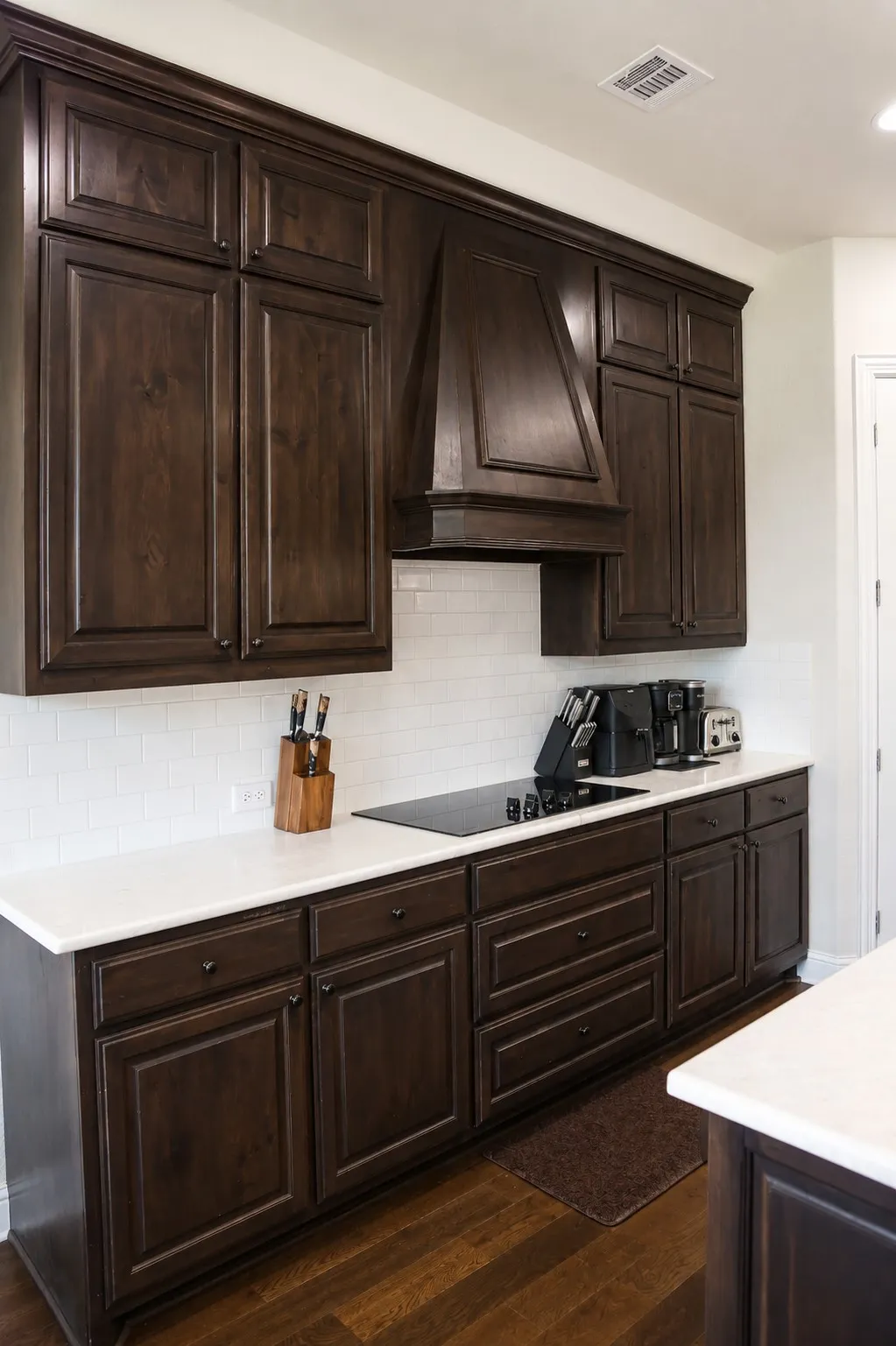 Kitchen featuring dark wood-finish cabinetry, white countertops, a subway tile backsplash, and a built-in cooktop