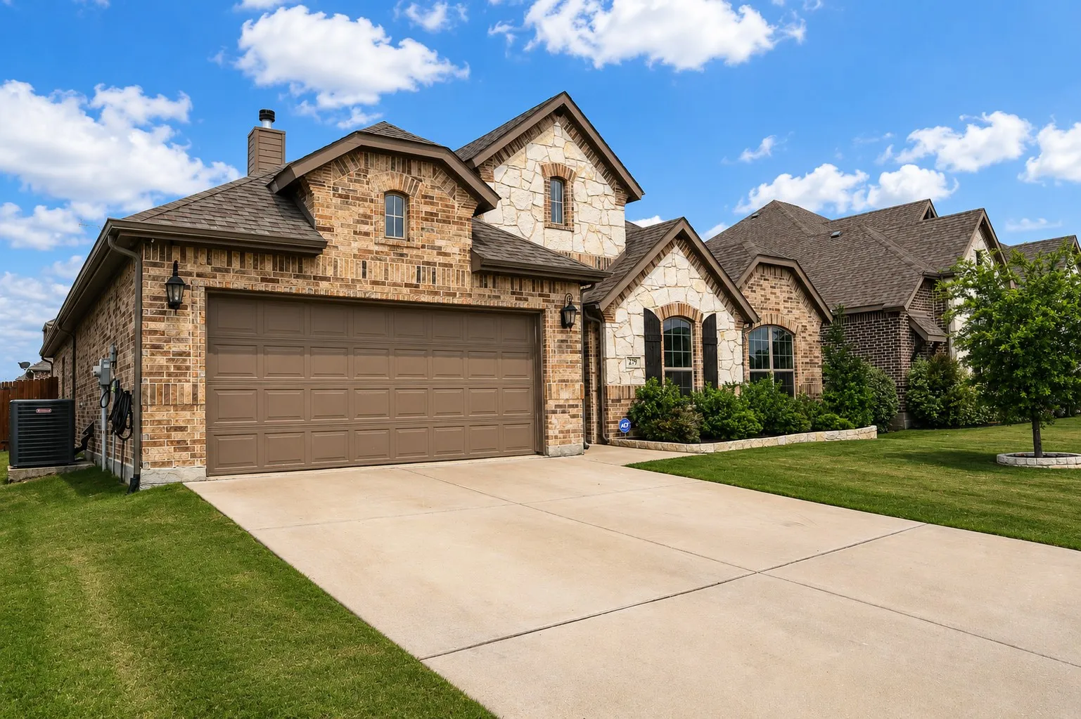 Brick and stone facade featuring a two-car garage, concrete driveway, and mature landscaping