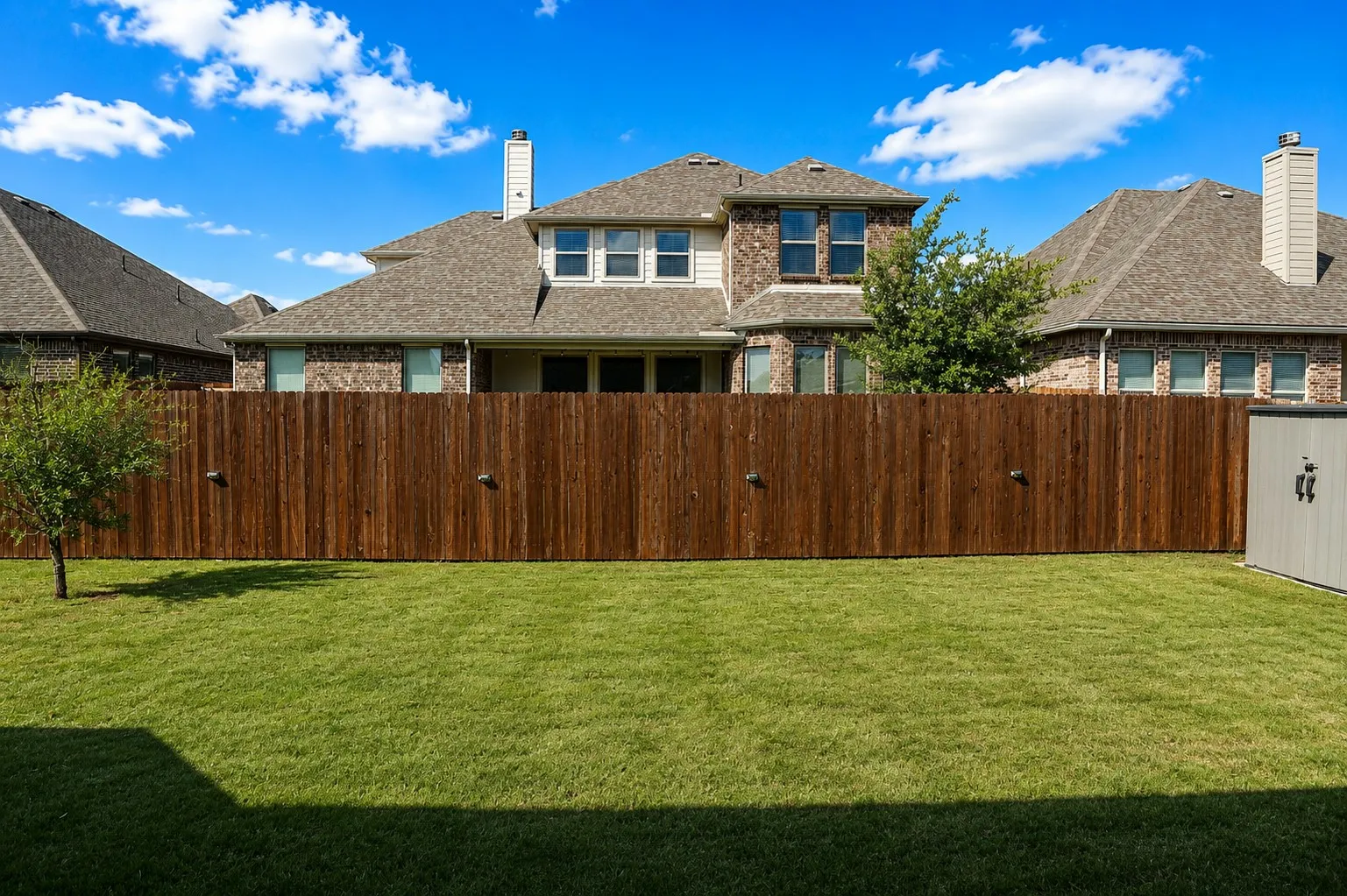 Expansive fenced backyard featuring a manicured lawn, full privacy fencing with integrated lighting, and a storage shed