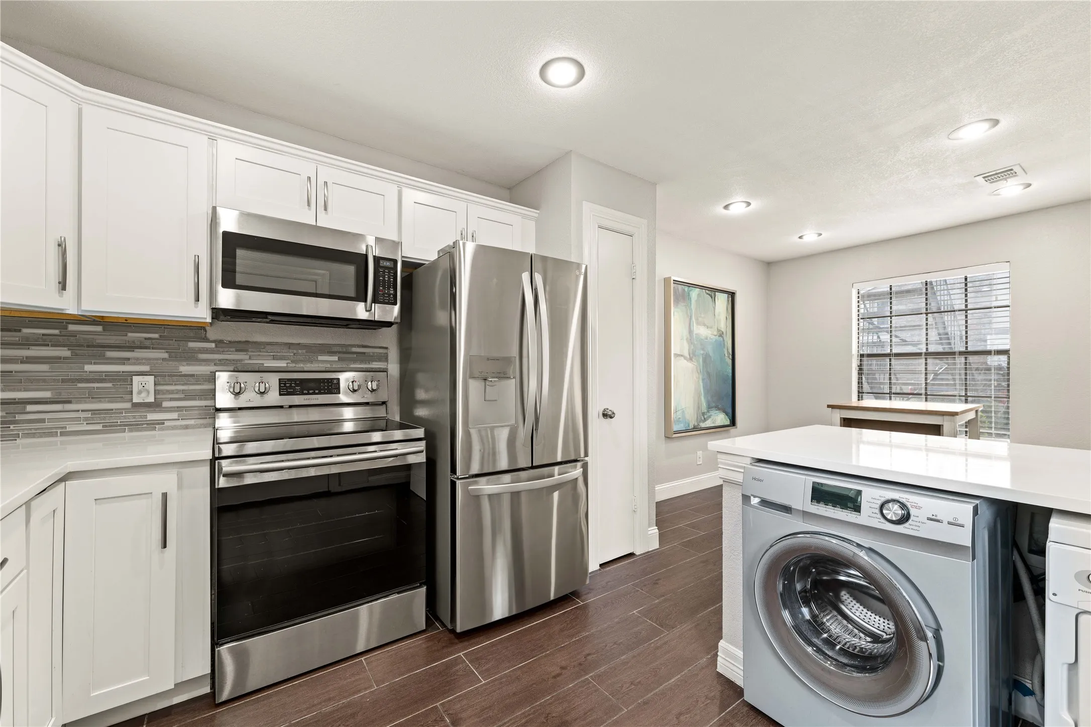 Modern kitchen featuring white shaker cabinetry, stainless steel appliances, a mosaic tile backsplash, and wood-finish flooring