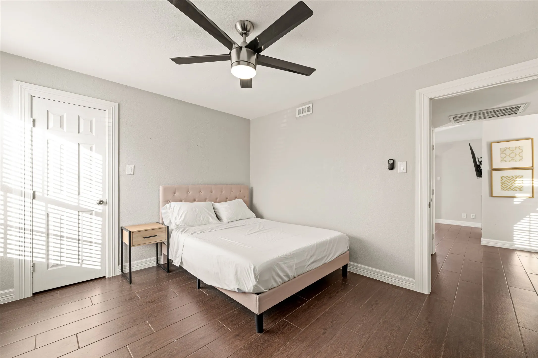 Spacious room featuring wood-finish flooring, light grey painted walls, a five-blade ceiling fan with integrated lighting, and a white paneled door