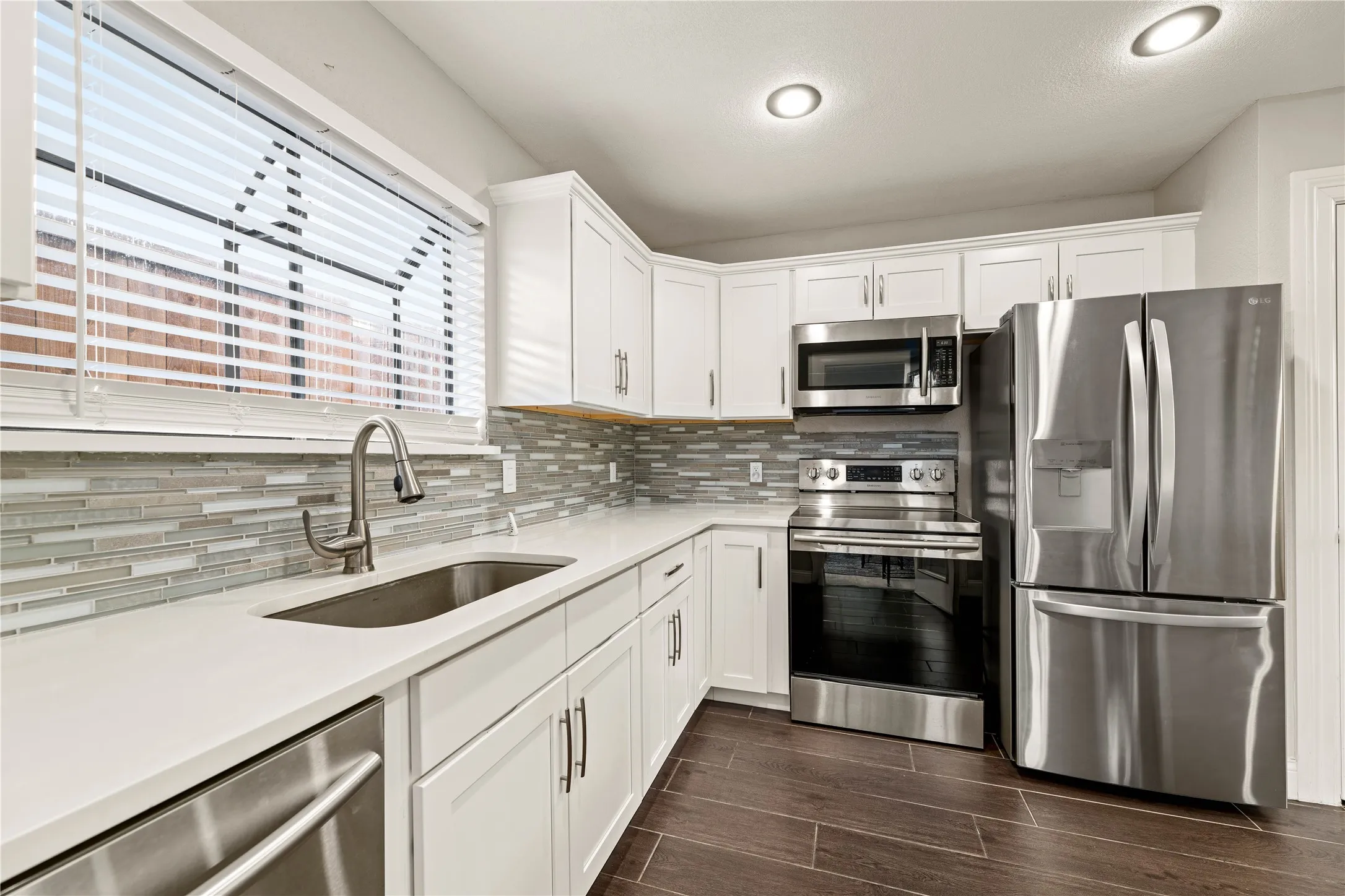 Modern kitchen featuring white cabinetry, stainless steel appliances, a mosaic tile backsplash, white countertops, and wood-finish flooring