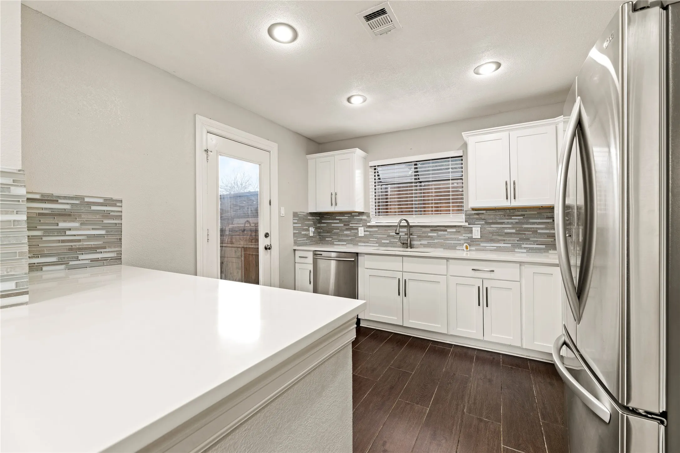 Contemporary kitchen featuring white cabinetry, stainless steel appliances, a mosaic tile backsplash, and dark wood-finish flooring