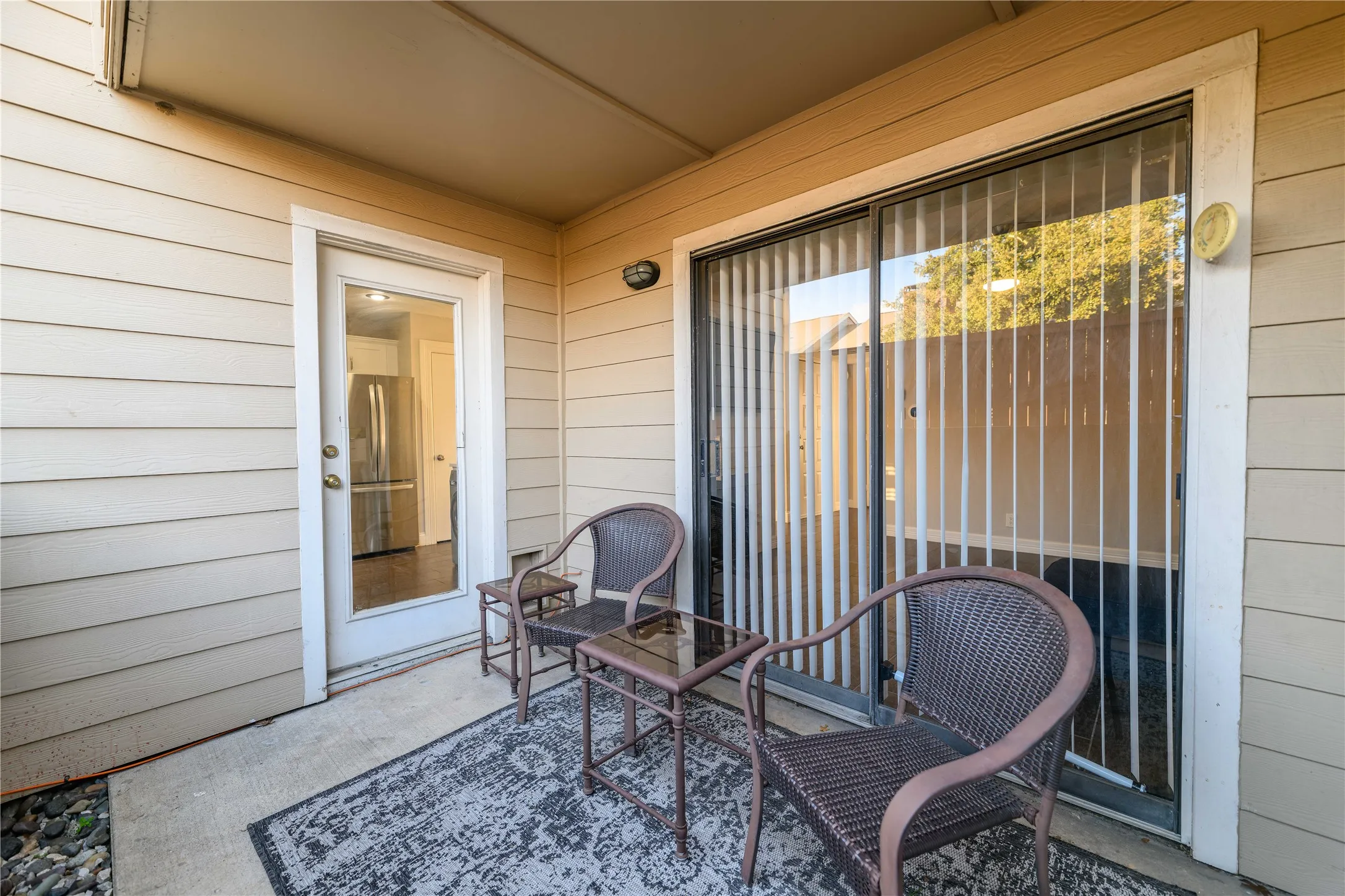 Covered patio featuring concrete flooring, a full-light exterior door, and a sliding glass door with vertical blinds