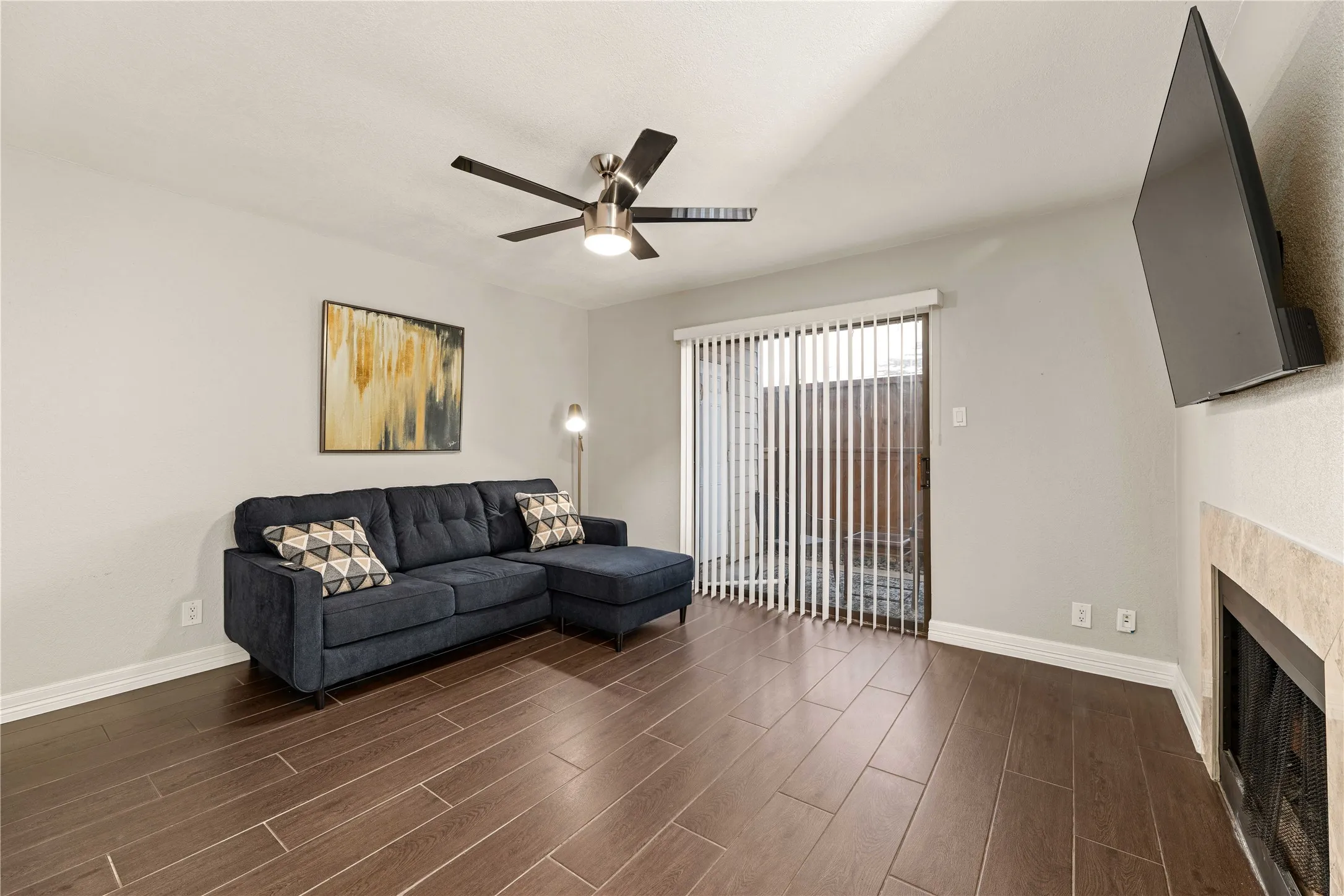 Living area featuring wood-finish flooring, a ceiling fan with integrated lighting, and a beige stone-clad fireplace
