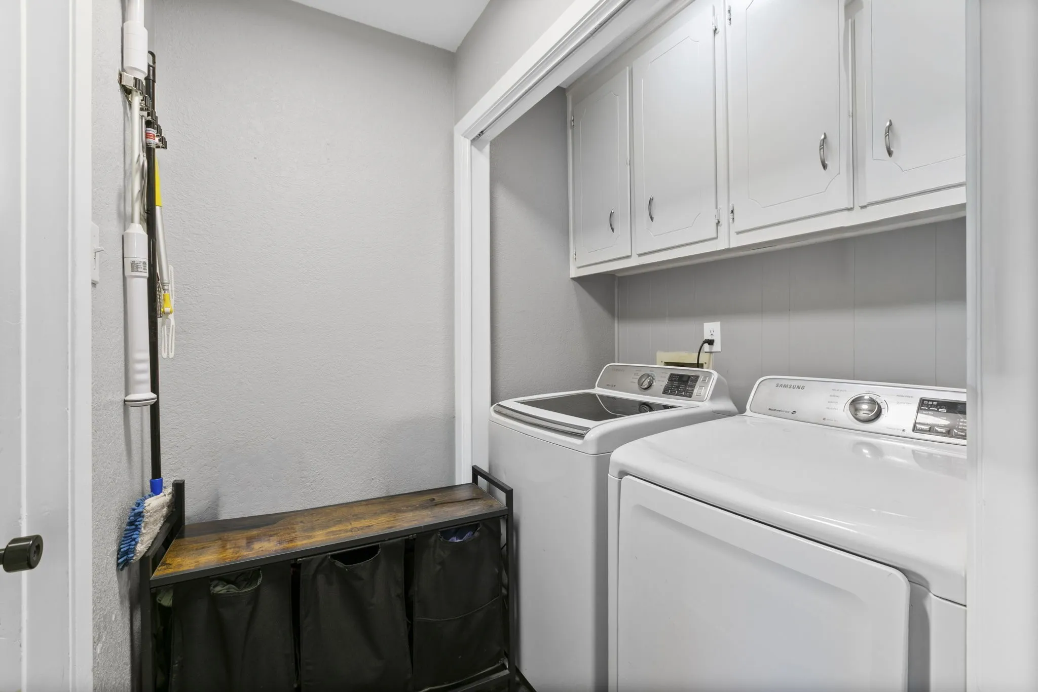 Dedicated laundry area featuring upper white cabinetry, beadboard wainscoting, and light gray wall paint