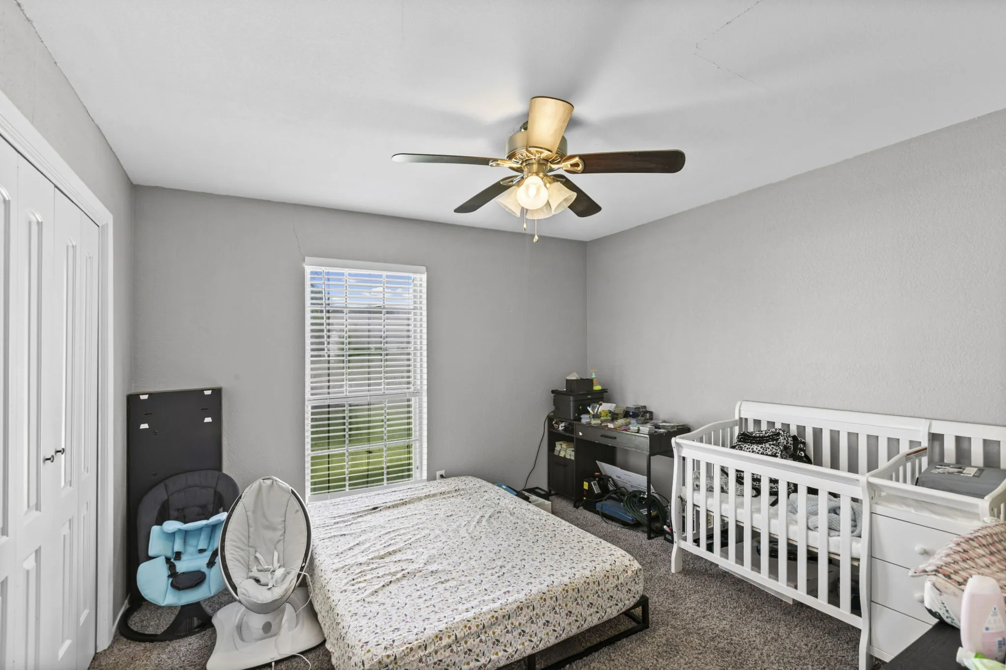 Carpeted room featuring a ceiling fan with light fixture, a window with horizontal blinds, and a built-in closet with white bifold doors