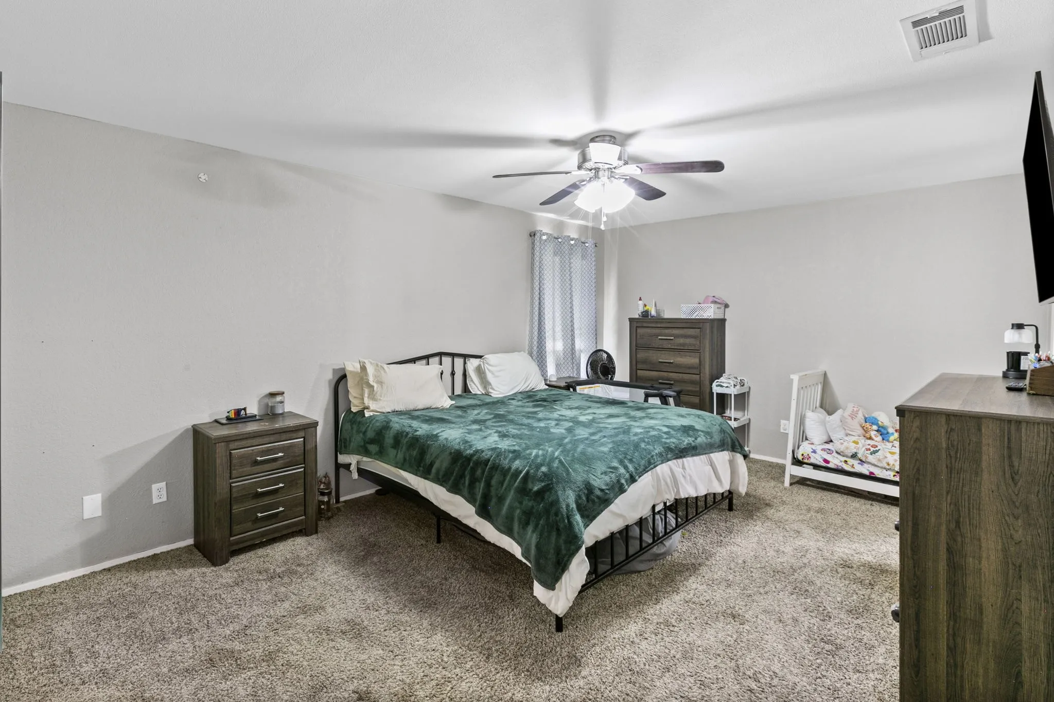 Spacious bedroom featuring neutral wall tones, textured carpet flooring, and a ceiling fan with integrated lighting