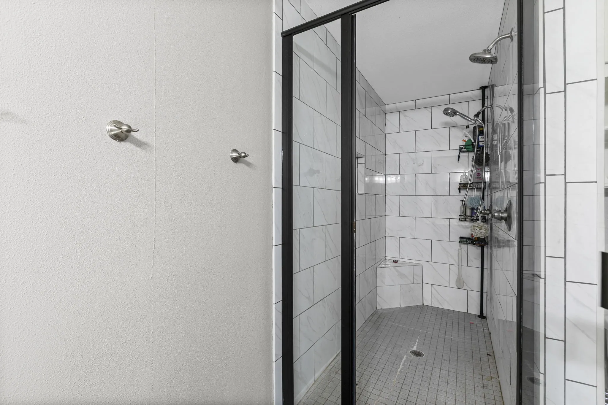 Shower enclosure with black-framed glass, white subway tile walls, a built-in bench, and a square tile floor