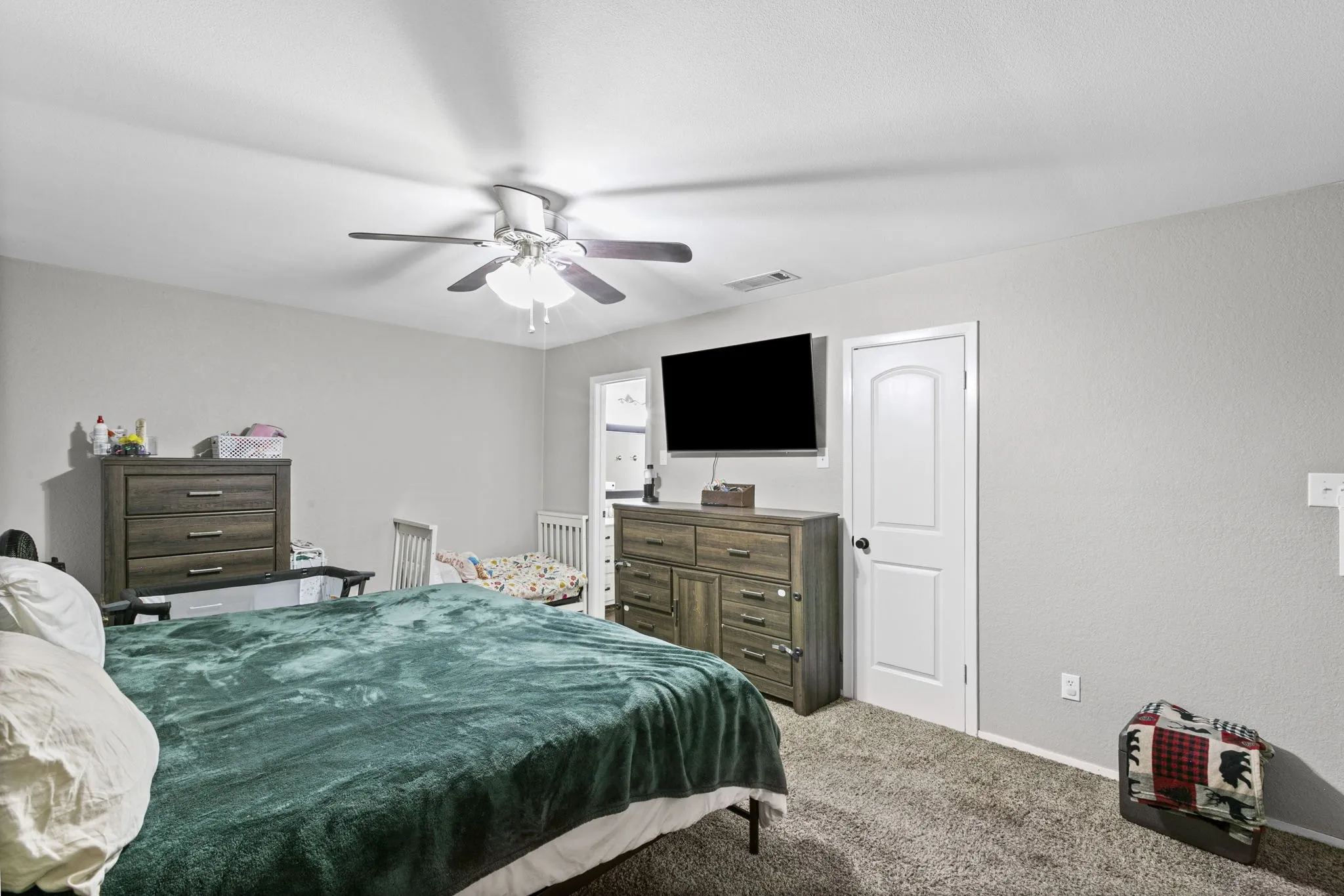 Spacious room featuring neutral-toned walls, textured carpet flooring, a ceiling fan with integrated lighting, and a white interior door with an arched panel design