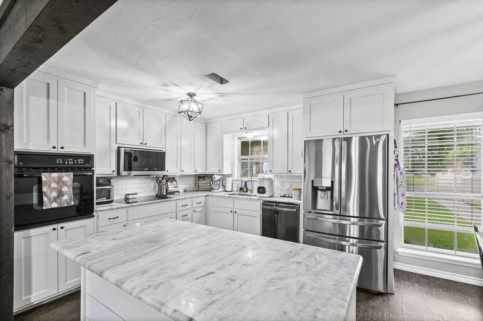 Kitchen featuring white shaker-style cabinetry, wood-finish flooring, stainless steel appliances, a center island with a stone countertop, and a tiled backsplash