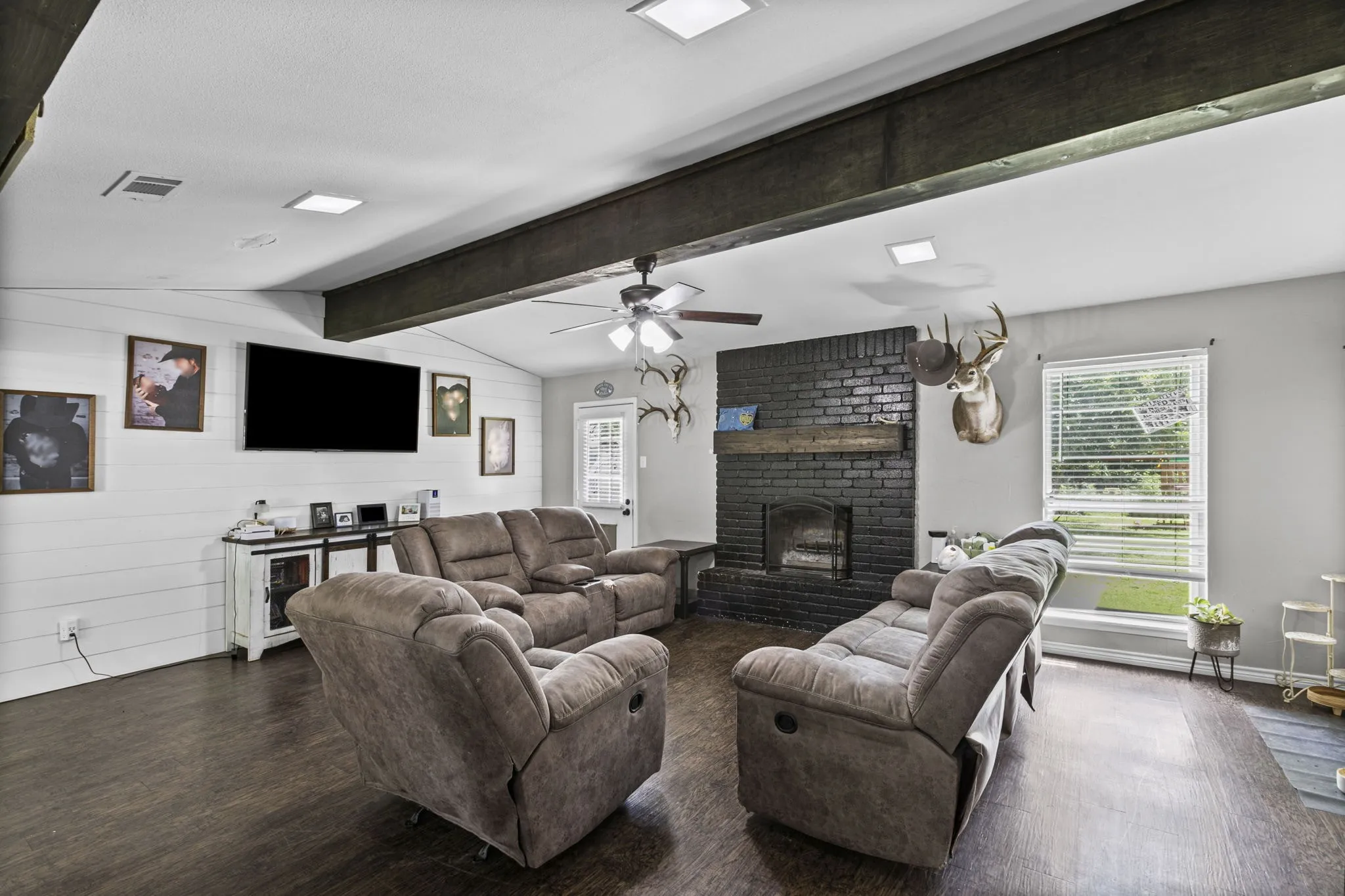 Living area featuring exposed wood beams, wood-finish flooring, and a black brick fireplace