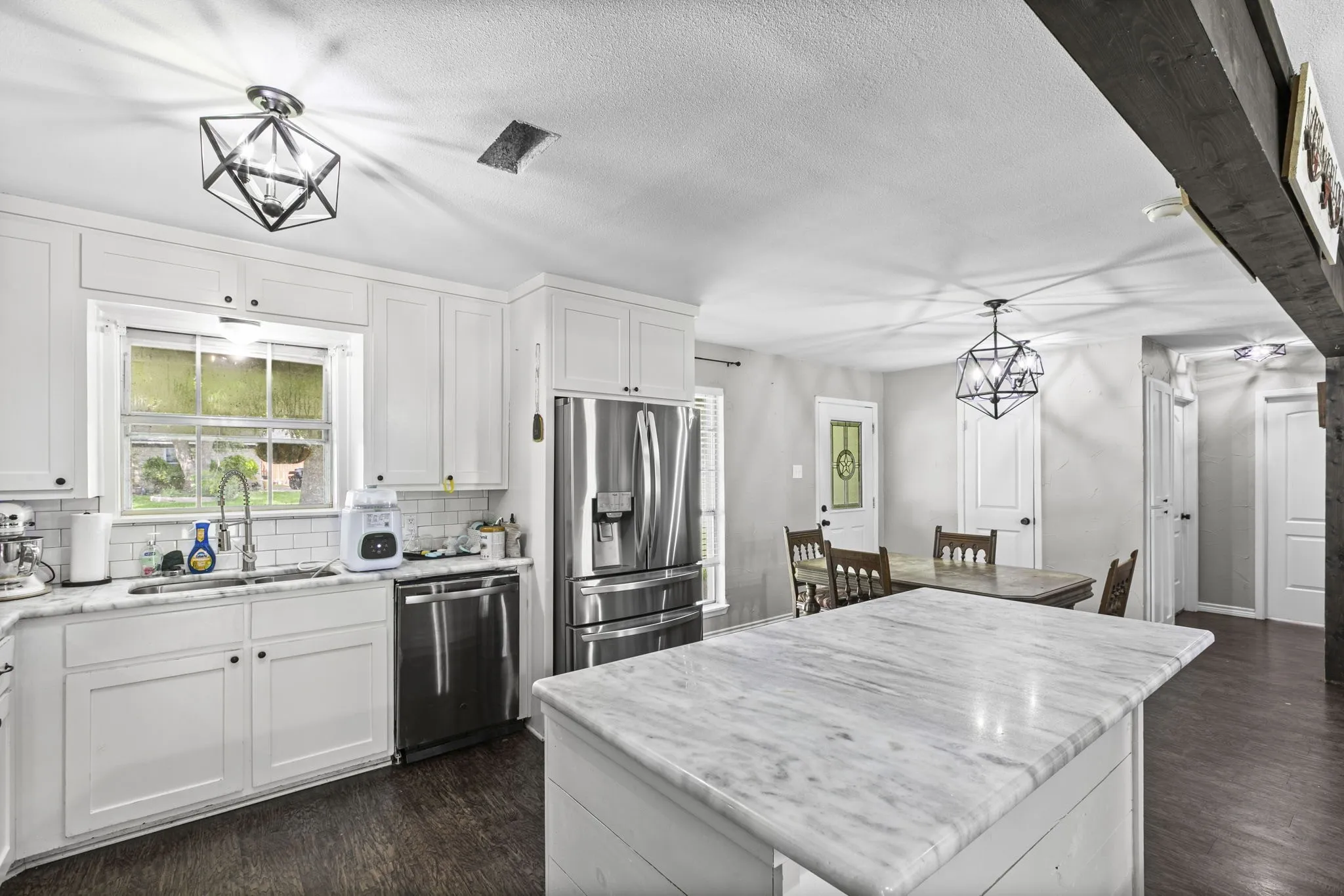 Kitchen featuring an island with a stone countertop, white cabinetry, undermount sink, stainless steel appliances, and dark wood-finish flooring