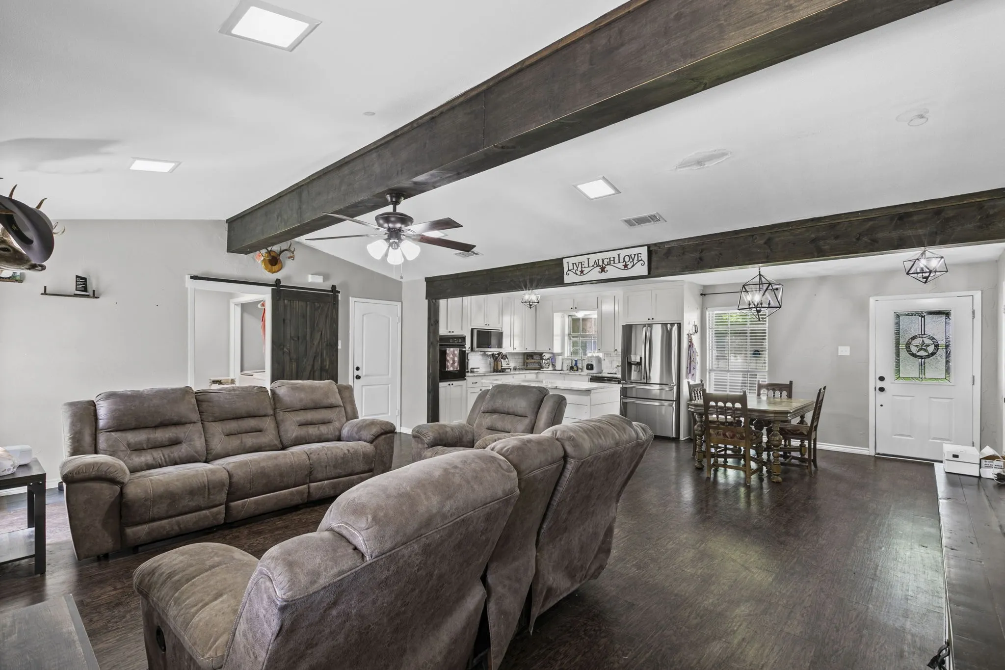 Open-concept living space with dark wood-finish flooring, exposed ceiling beams, and recessed lighting