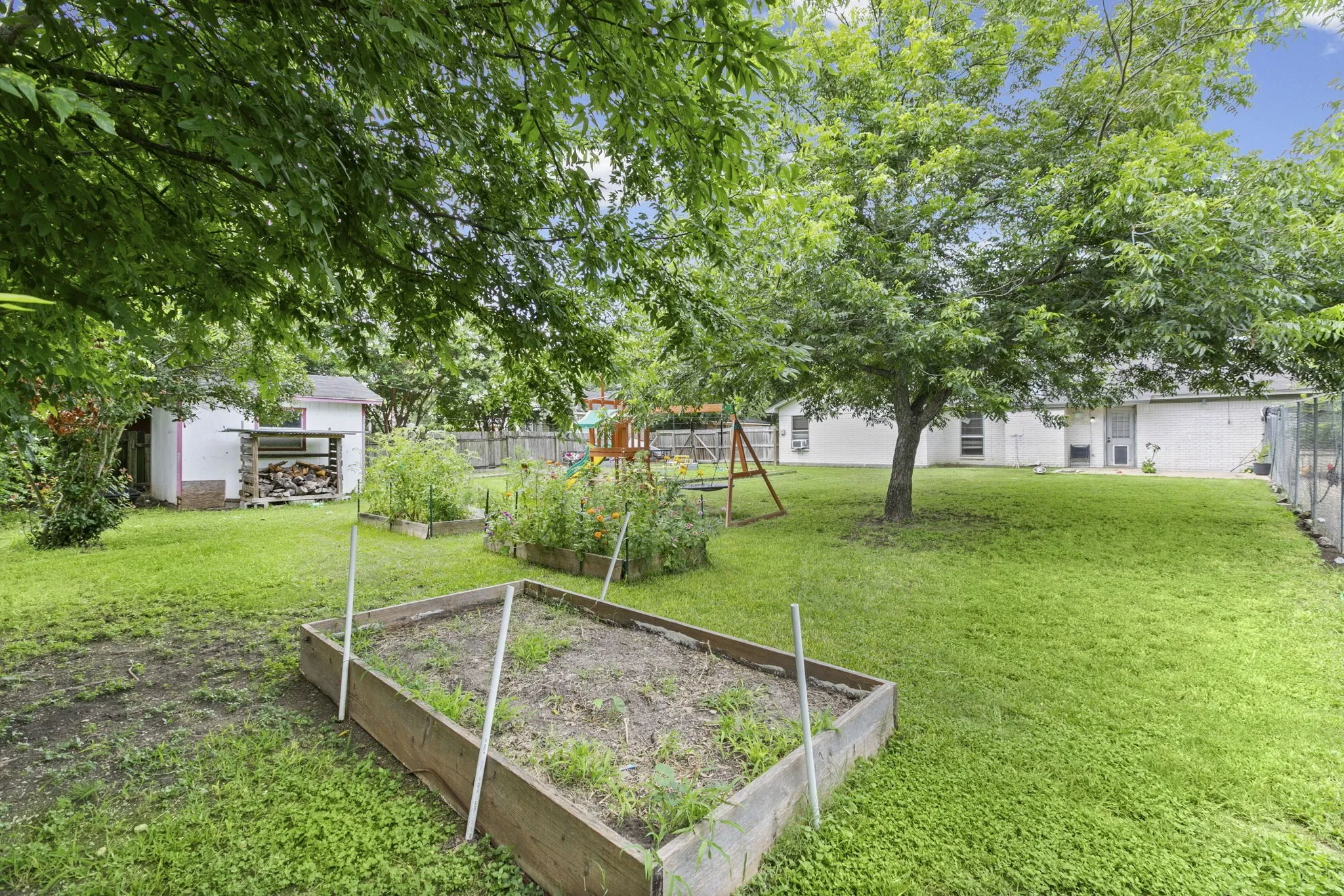 Expansive backyard featuring a large tree, raised garden beds, a storage shed, and perimeter fencing