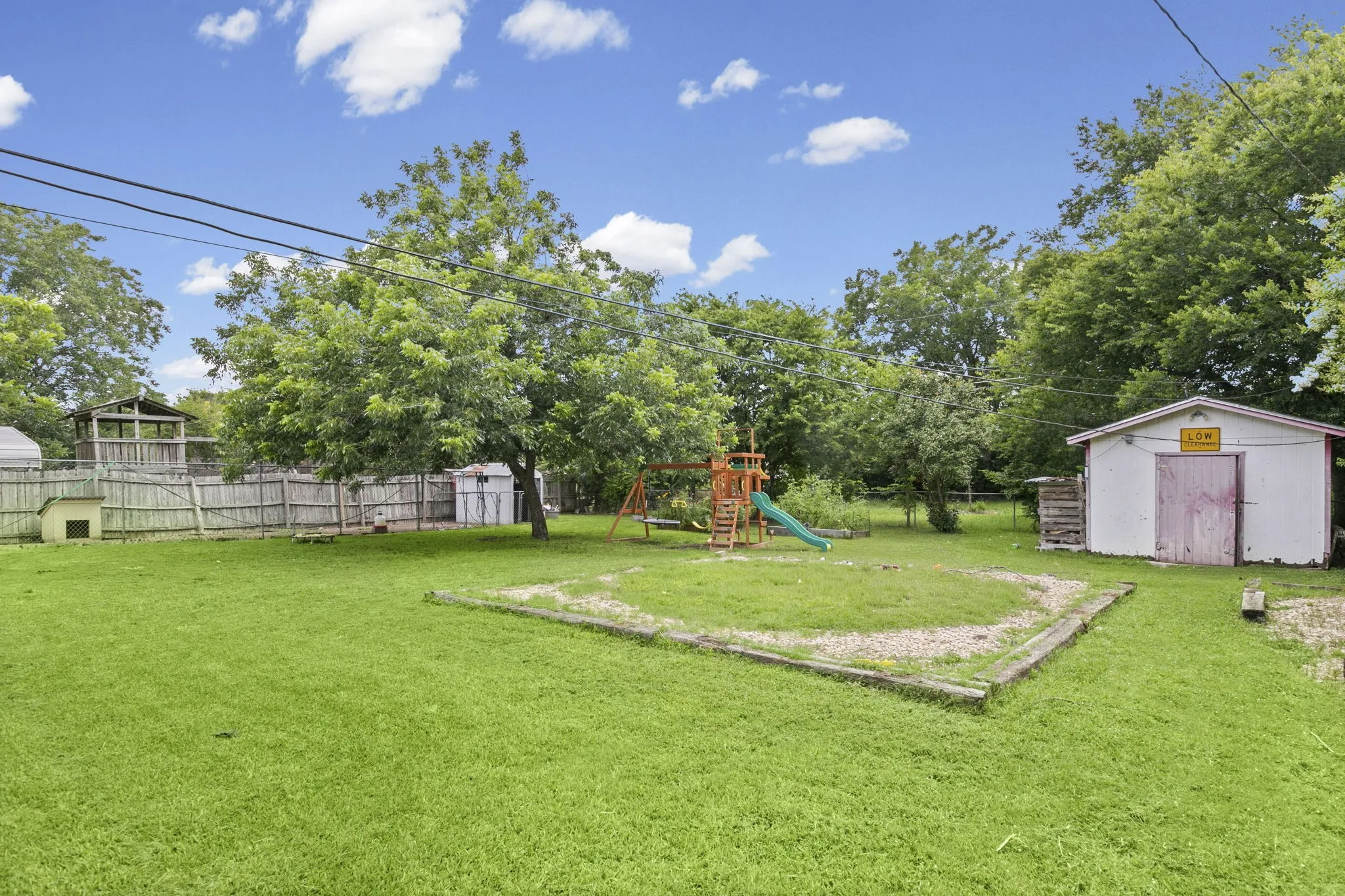 Expansive fenced backyard featuring a grassy lawn, mature trees, a storage shed, and a sandpit area