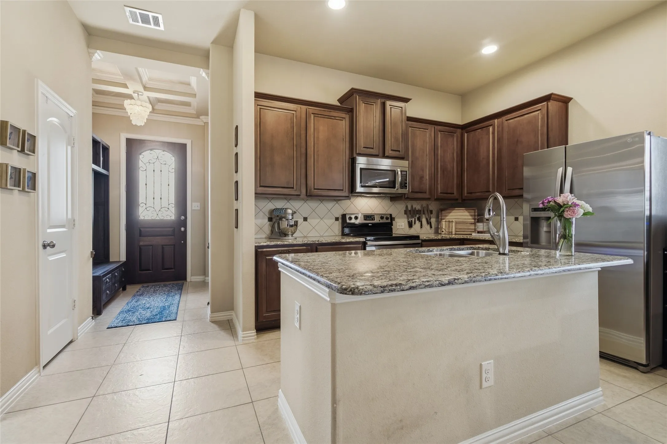 Open-concept kitchen featuring an island with a built-in sink, wood-finish cabinetry, stainless steel appliances, and a tiled backsplash