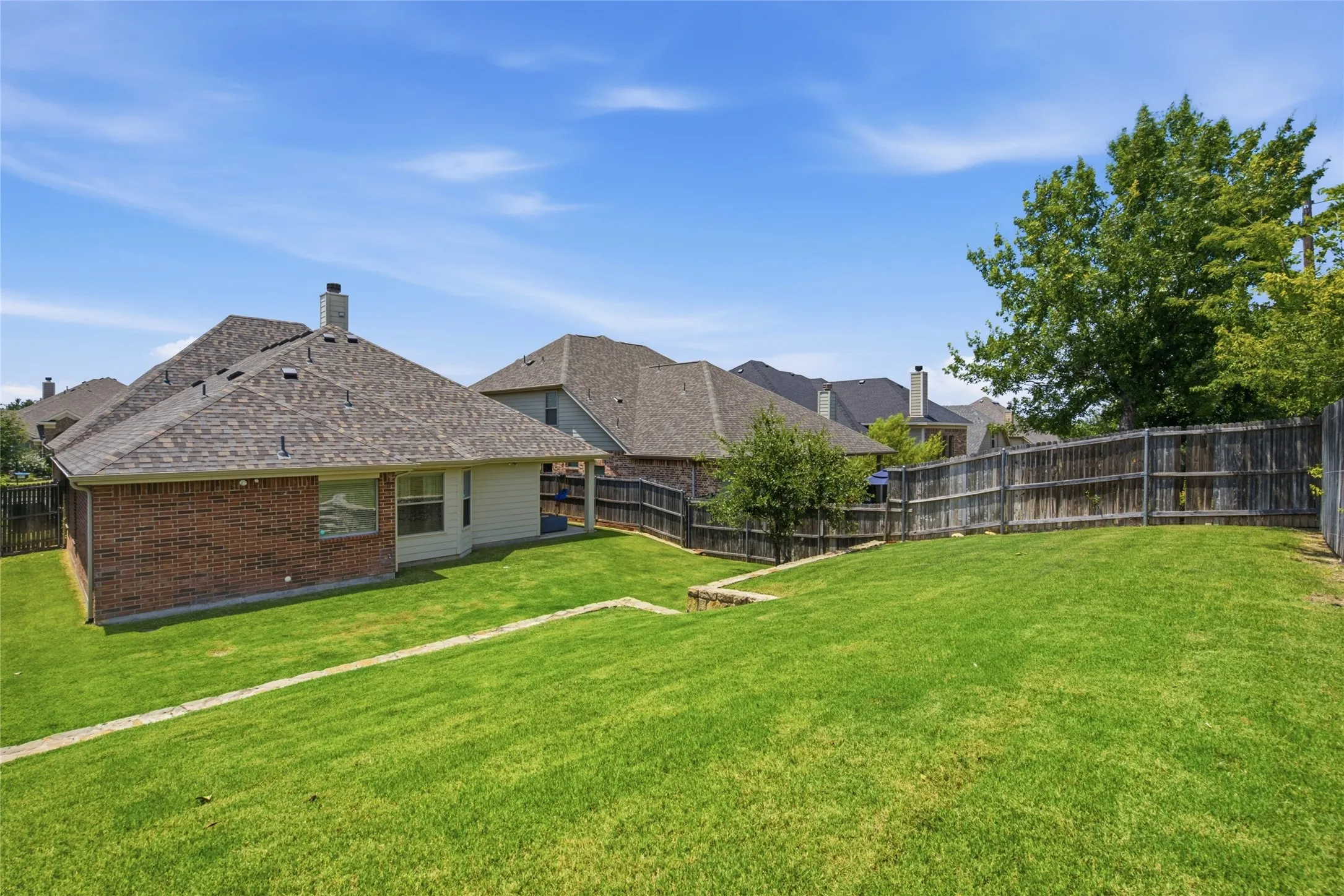 Expansive rear yard featuring a sloped lawn, privacy fencing, and mature trees