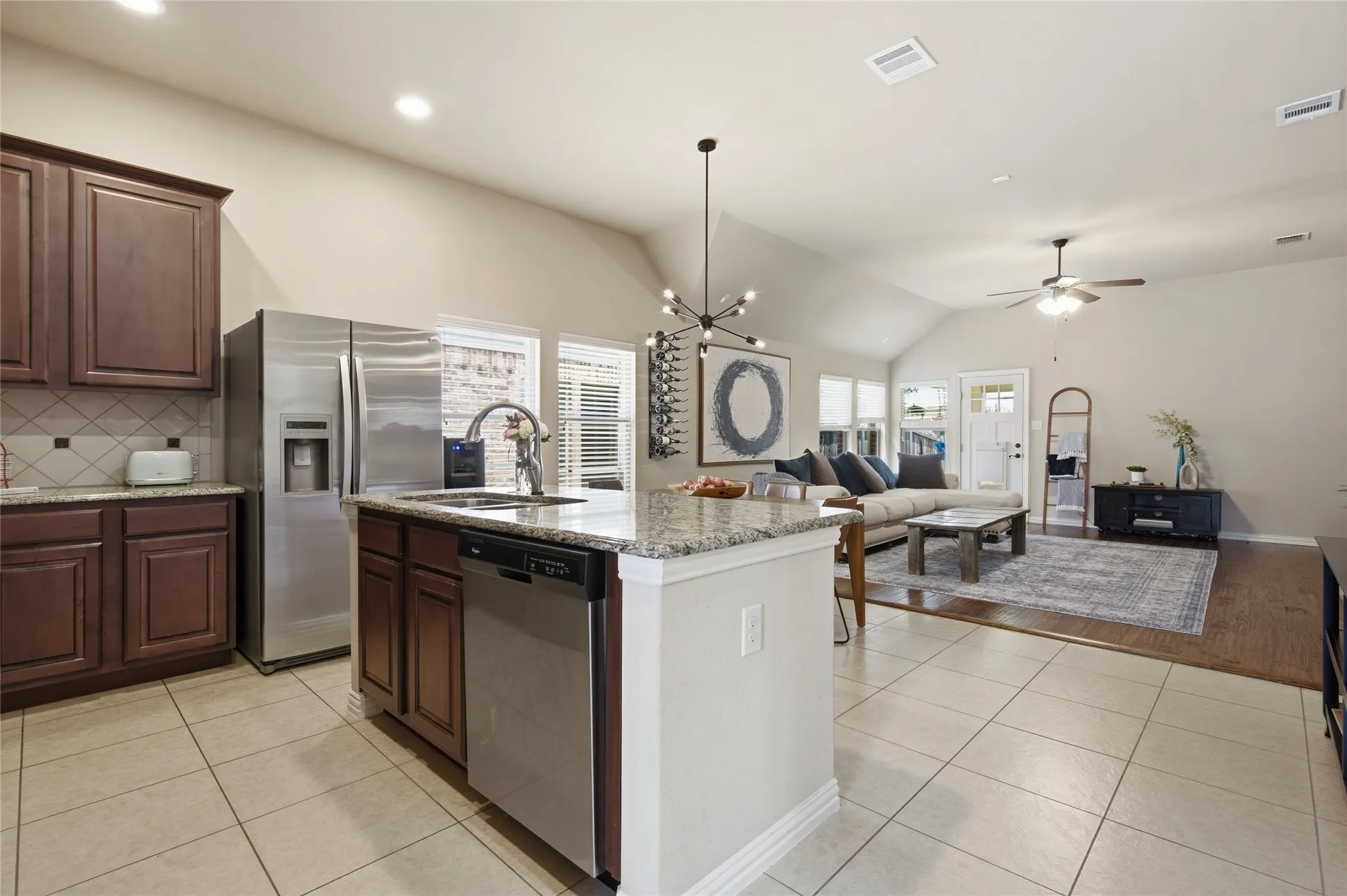 Kitchen featuring an island with a granite countertop, stainless steel appliances, wood cabinetry, and tile flooring