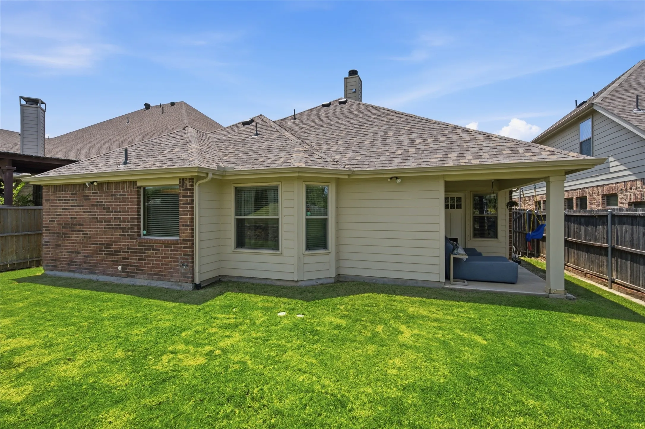Expansive rear lawn featuring a covered patio, brick and siding exterior, and a shingled roof