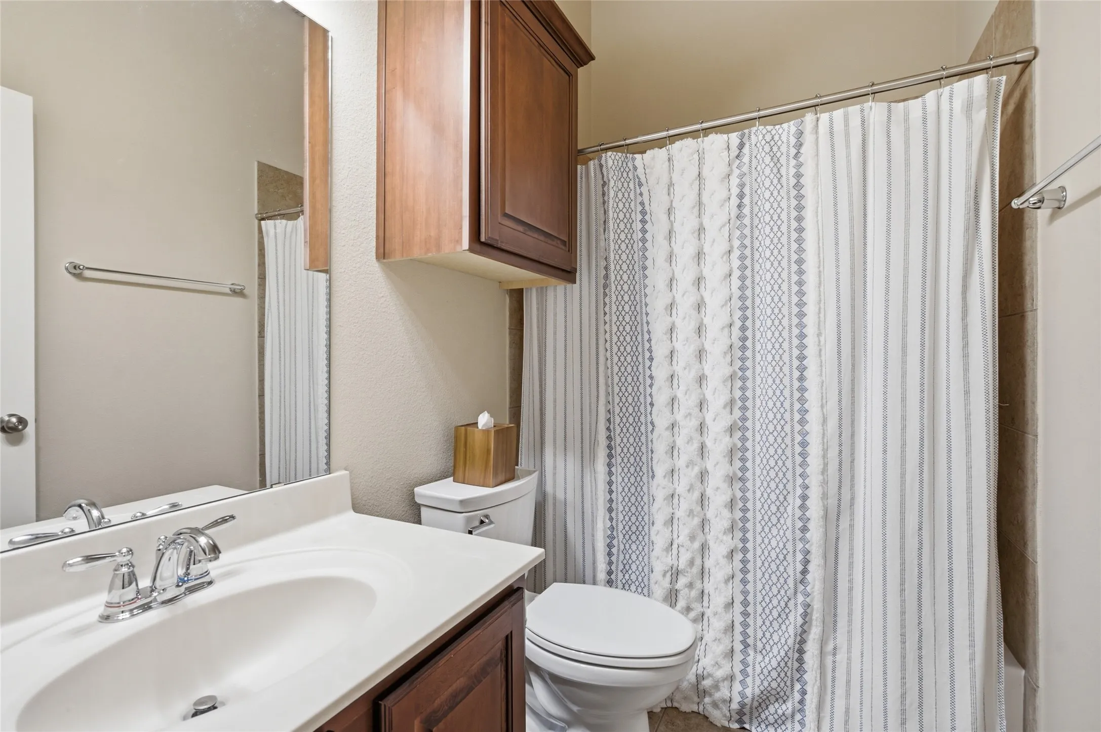 Bathroom featuring a vanity with a white countertop and dark wood-finish cabinetry, chrome fixtures, a shower/tub combination with tiled surround, and a wall-mounted storage cabinet
