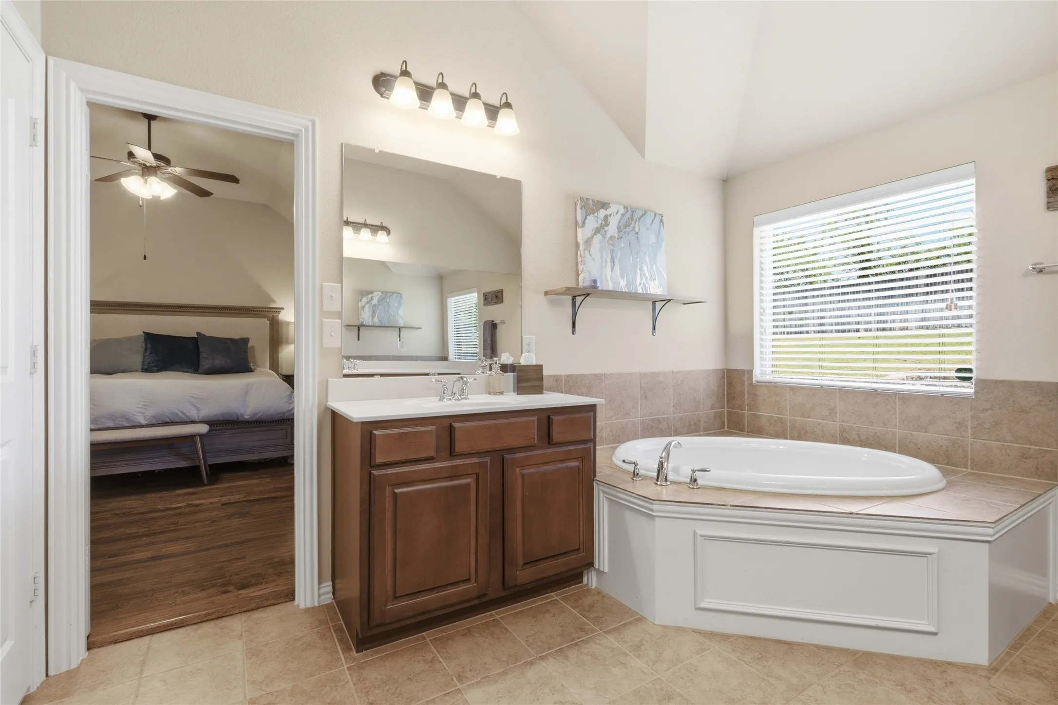 Bathroom featuring a built-in soaking tub with tiled surround, a vanity with a white countertop and wood cabinetry, and tiled flooring