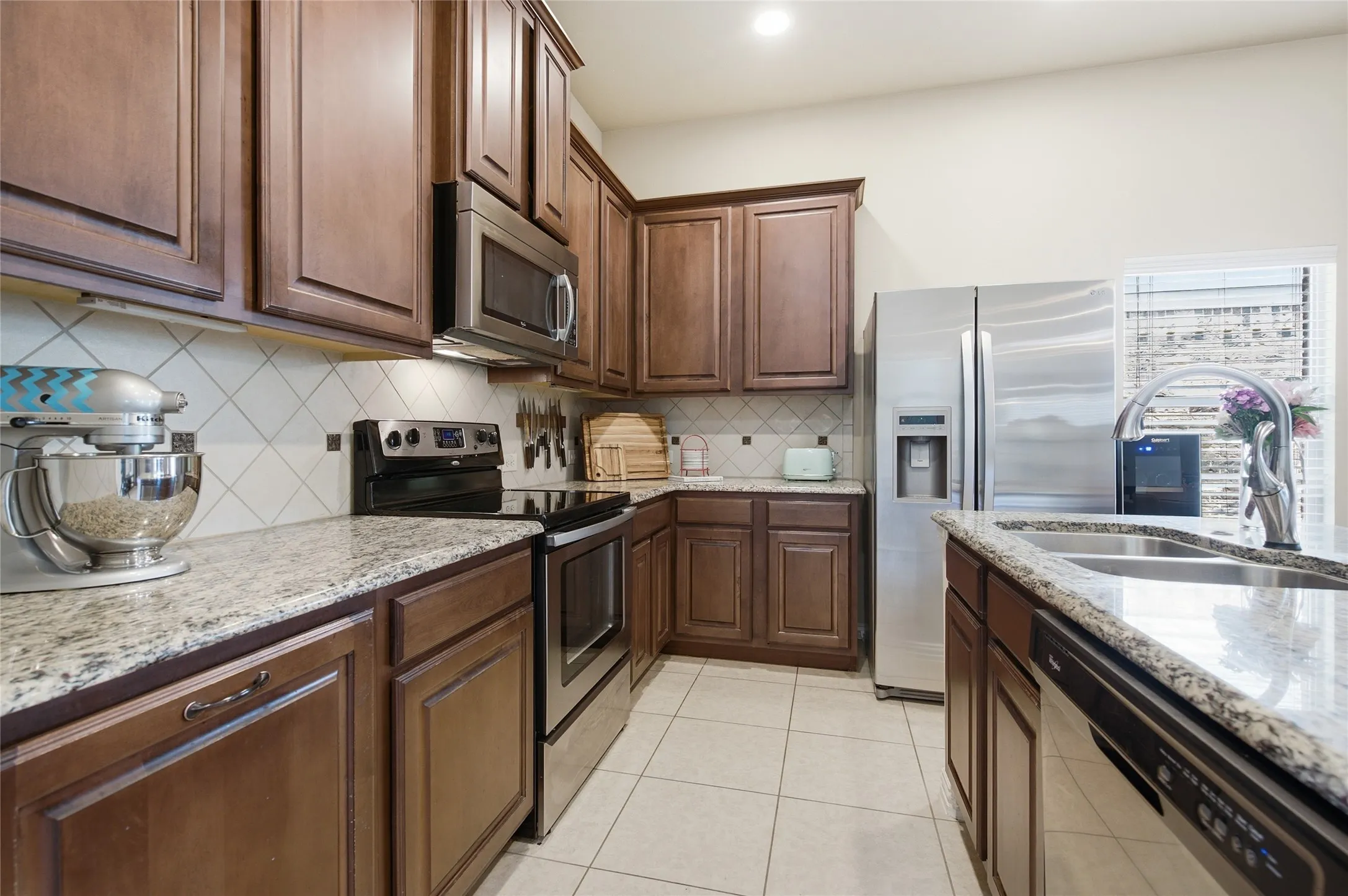 Kitchen featuring dark wood cabinetry, granite countertops, stainless steel appliances, a tile backsplash, and tile flooring