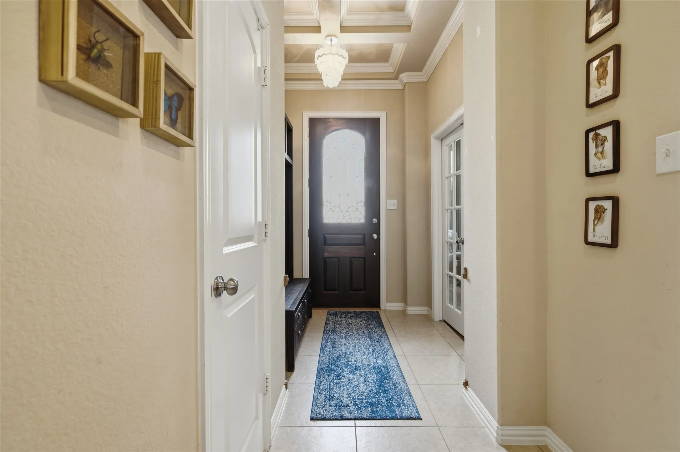 Entryway featuring a dark wood door with decorative glass, tiled flooring, white crown molding, and a coffered ceiling