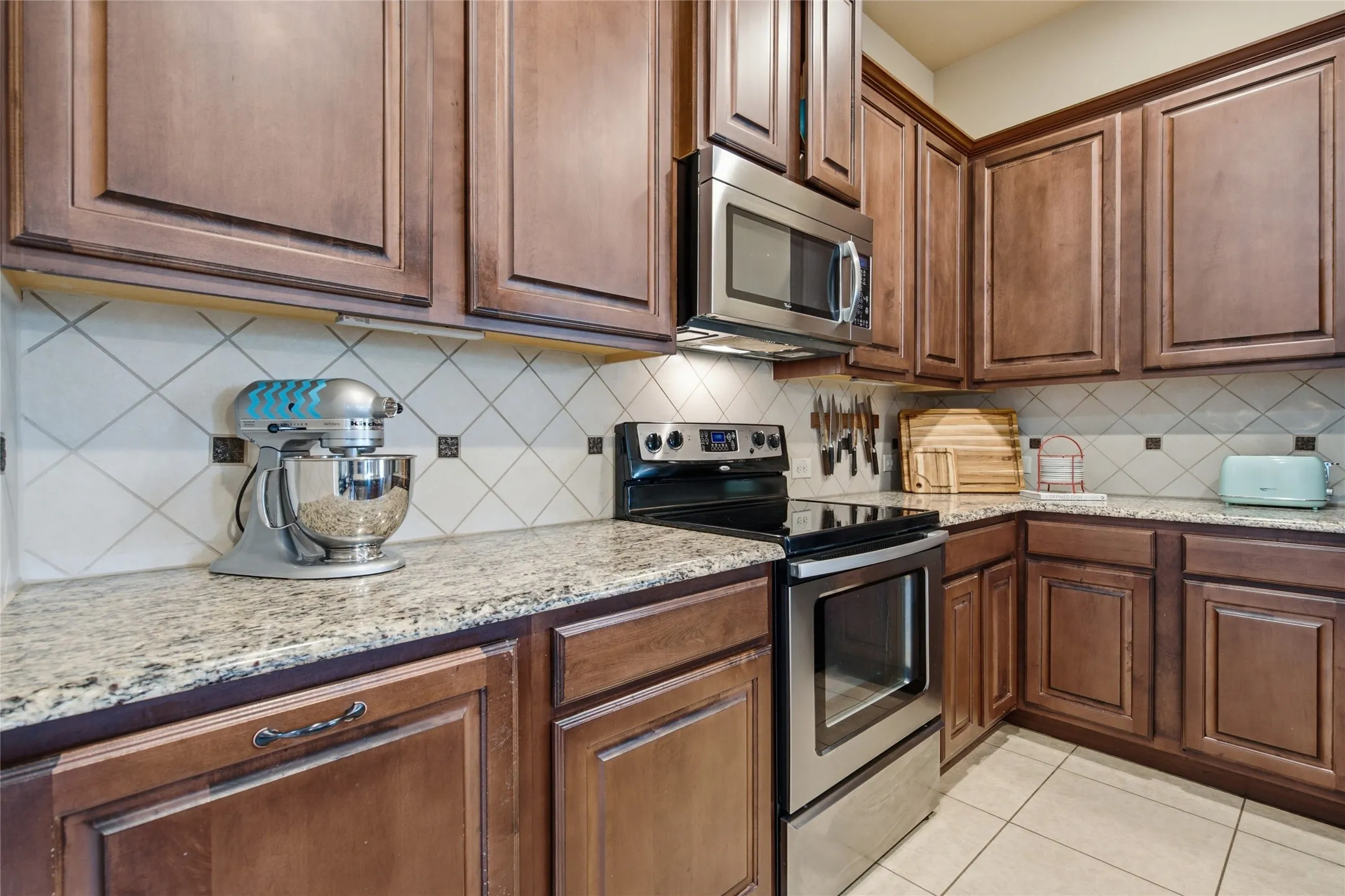 Kitchen featuring granite countertops, wood cabinetry, stainless steel appliances, a tile backsplash, and tile flooring