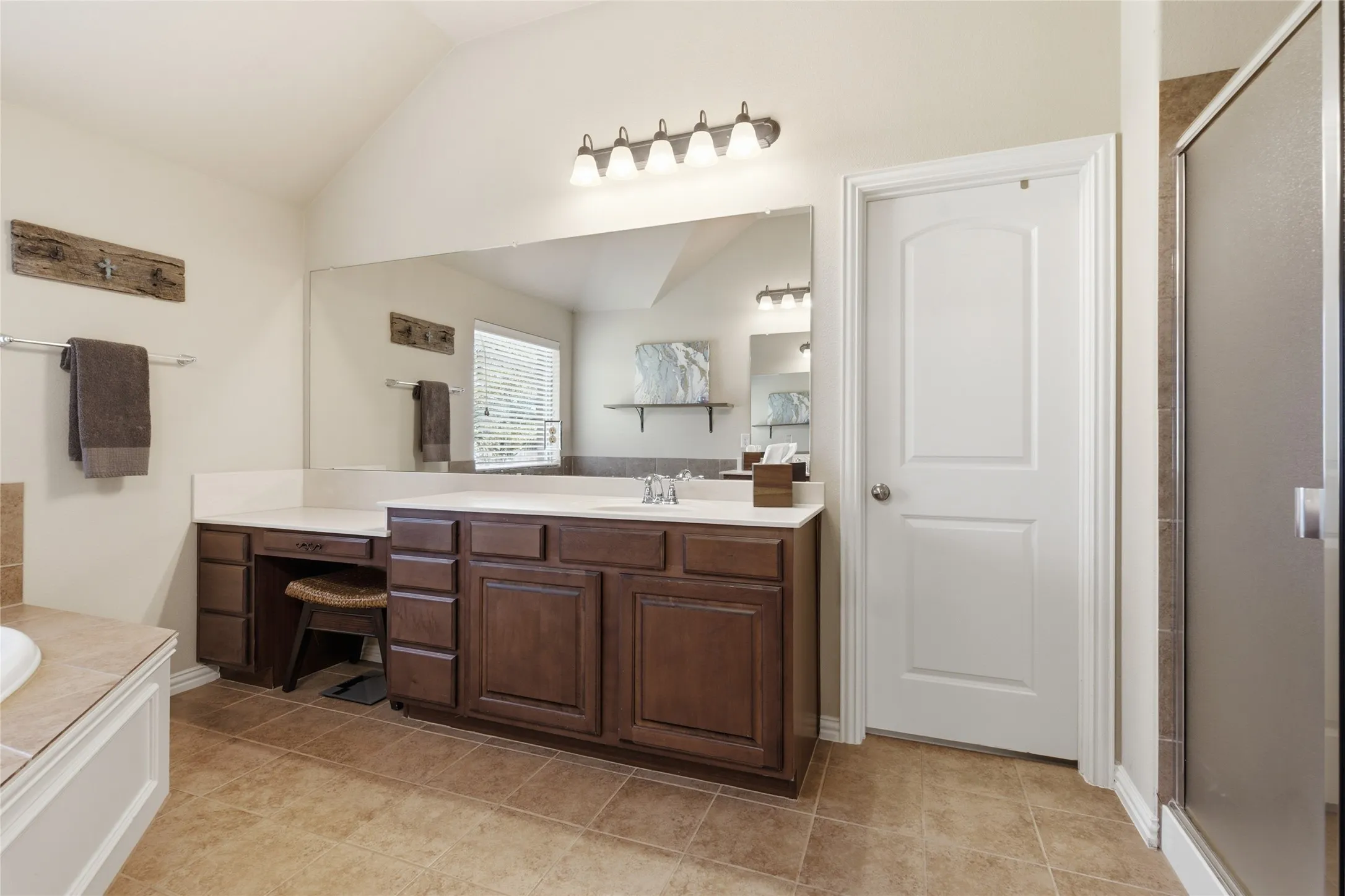 Separate vanities with wood cabinetry, integrated dressing area, and a large wall-mounted mirror