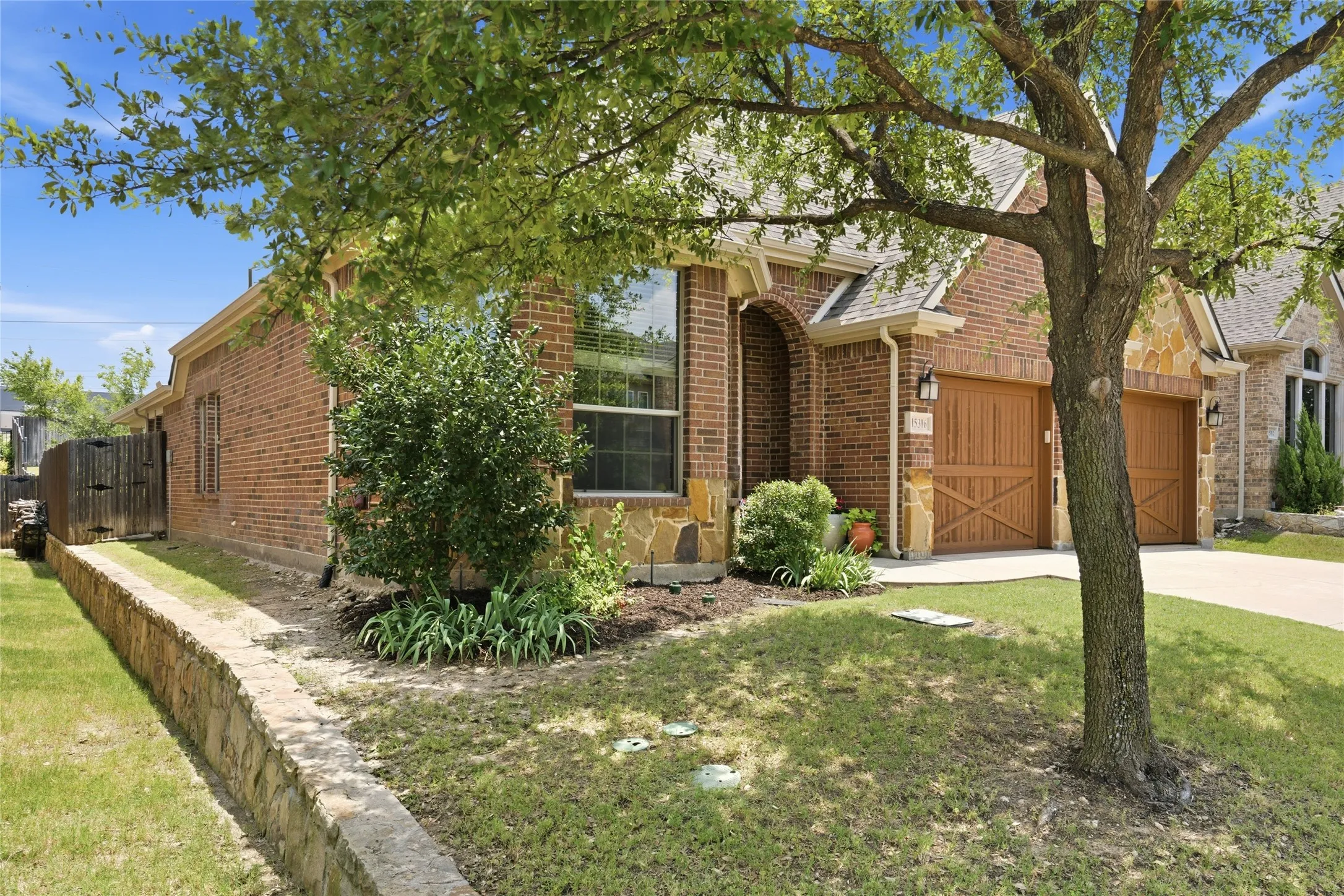 Brick and stone exterior featuring an arched entry, wood-paneled garage doors, and a stone retaining wall