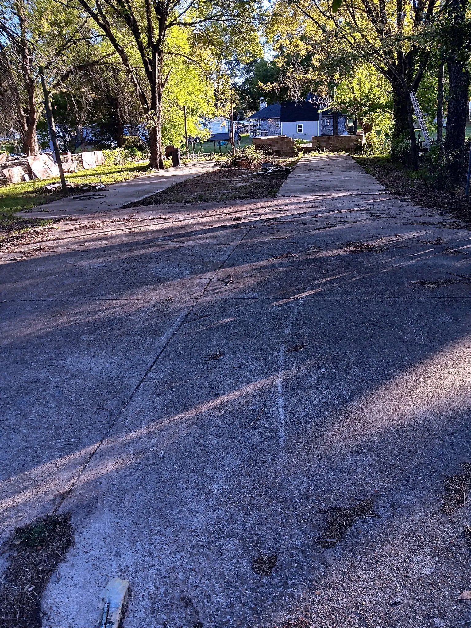 Paved driveway extending towards a residential structure, flanked by mature trees