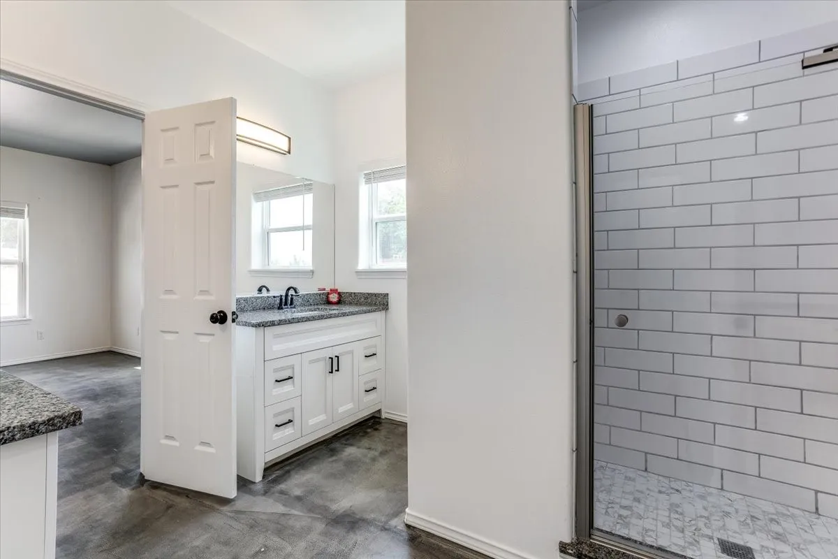 Bathroom featuring a double vanity with stone countertop, white cabinetry with dark hardware, and a fully enclosed shower with subway tile surround and mosaic floor