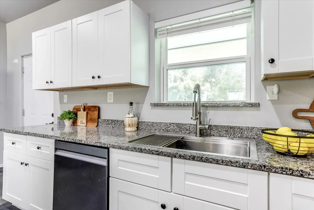 Kitchen featuring white shaker-style cabinetry, dark speckled countertops, and a stainless steel undermount sink with a gooseneck faucet