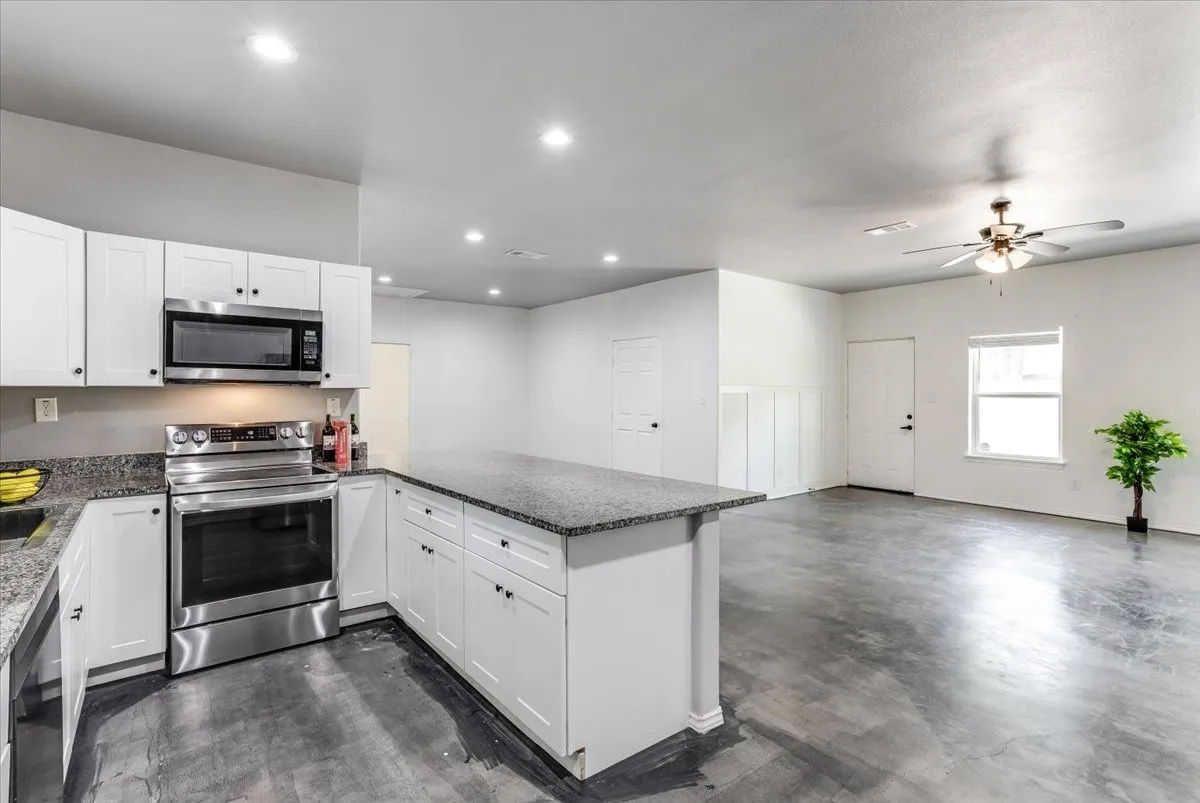 Open-concept kitchen and living area featuring white cabinetry, dark speckled countertops, and stainless steel appliances