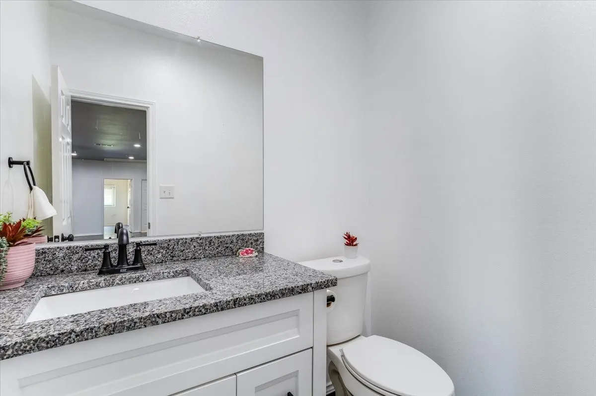 Bathroom featuring a white vanity with shaker-style cabinetry, a granite countertop, an undermount sink, and a black faucet