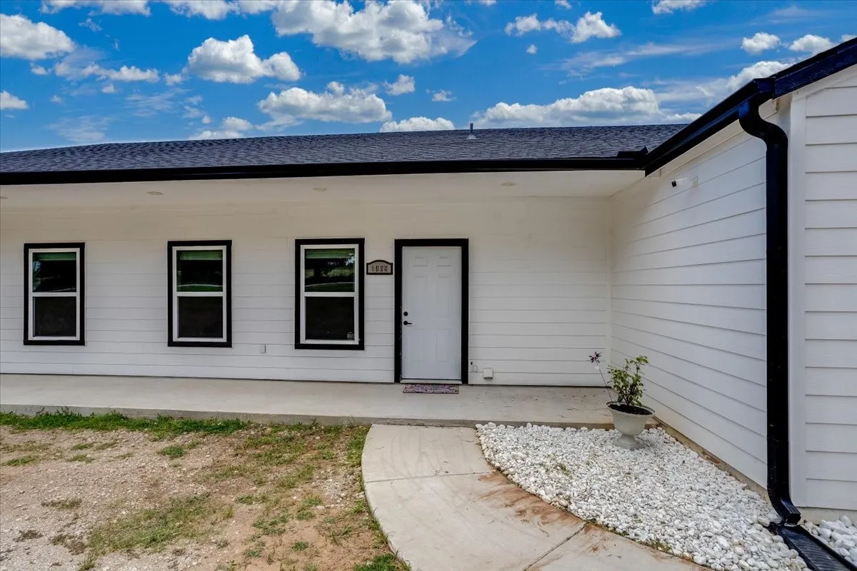 White horizontal siding exterior with black trim windows, a dark shingle roof, and a concrete pathway leading to the front entry