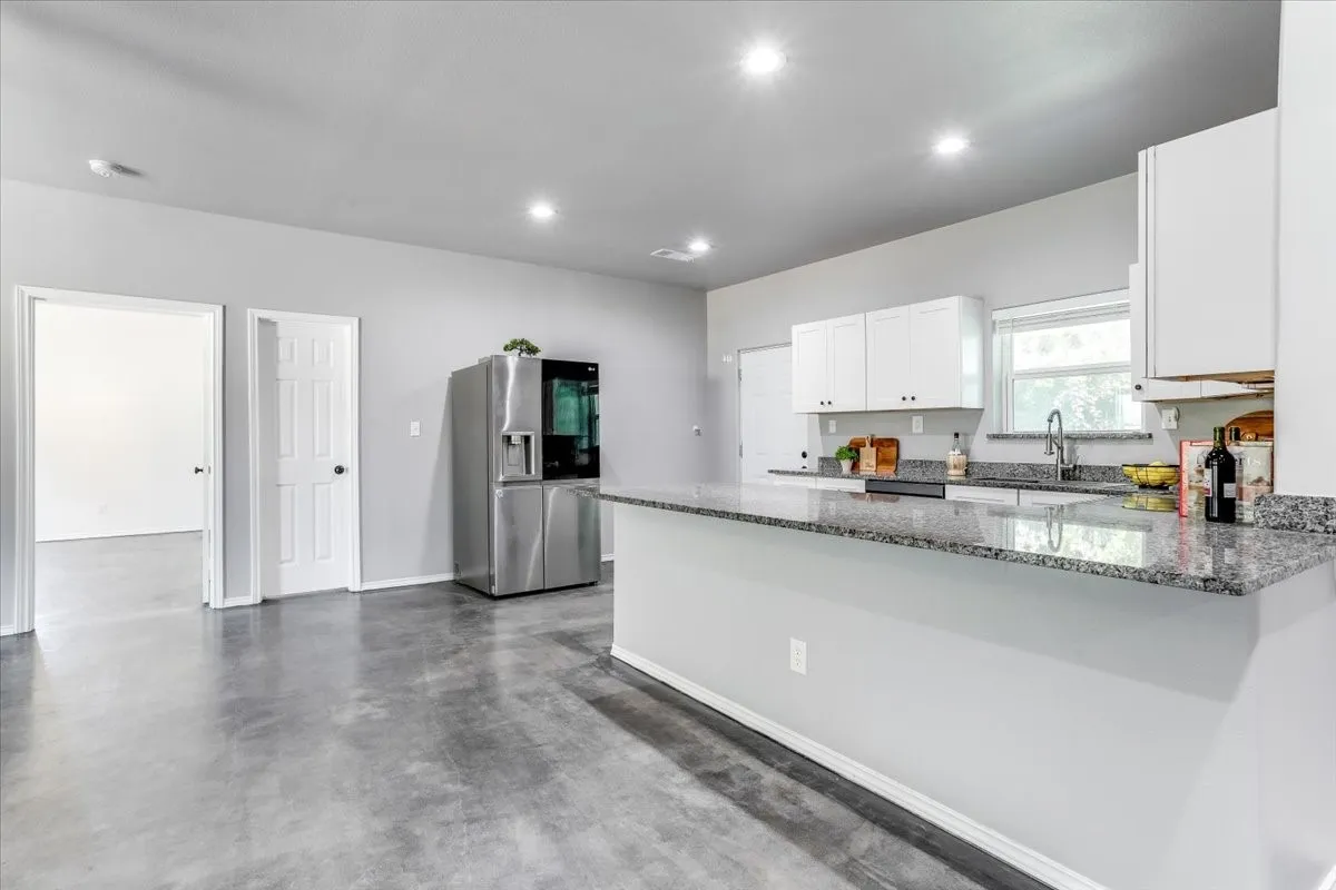 Modern kitchen featuring a granite-topped island with breakfast bar, white cabinetry, a stainless steel refrigerator, and recessed lighting
