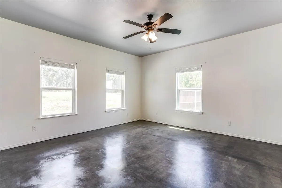 Spacious room featuring polished concrete flooring, white walls, and a ceiling fan with integrated lighting