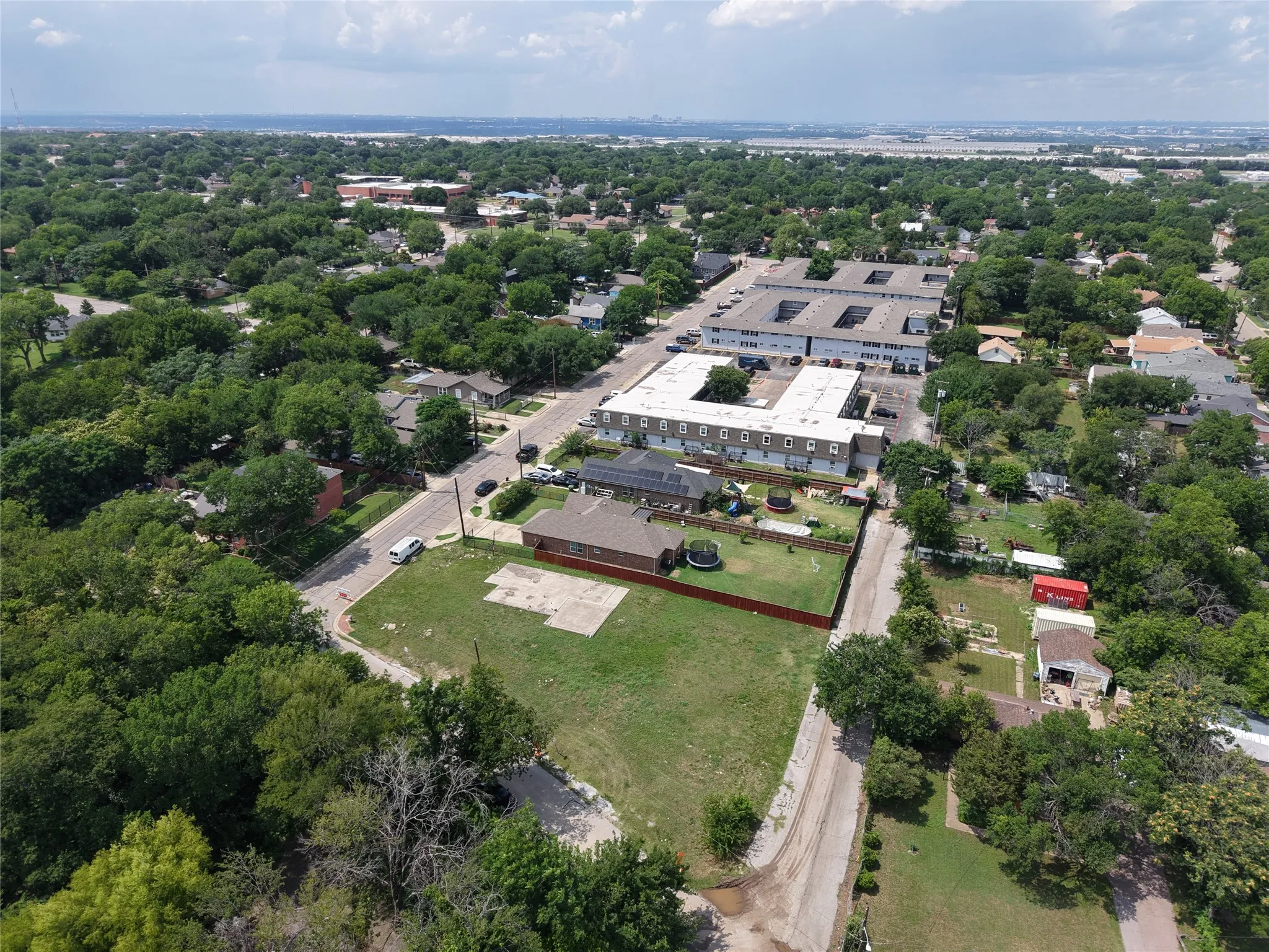 Expansive corner lot featuring a partial concrete slab, surrounded by mature trees and residential properties