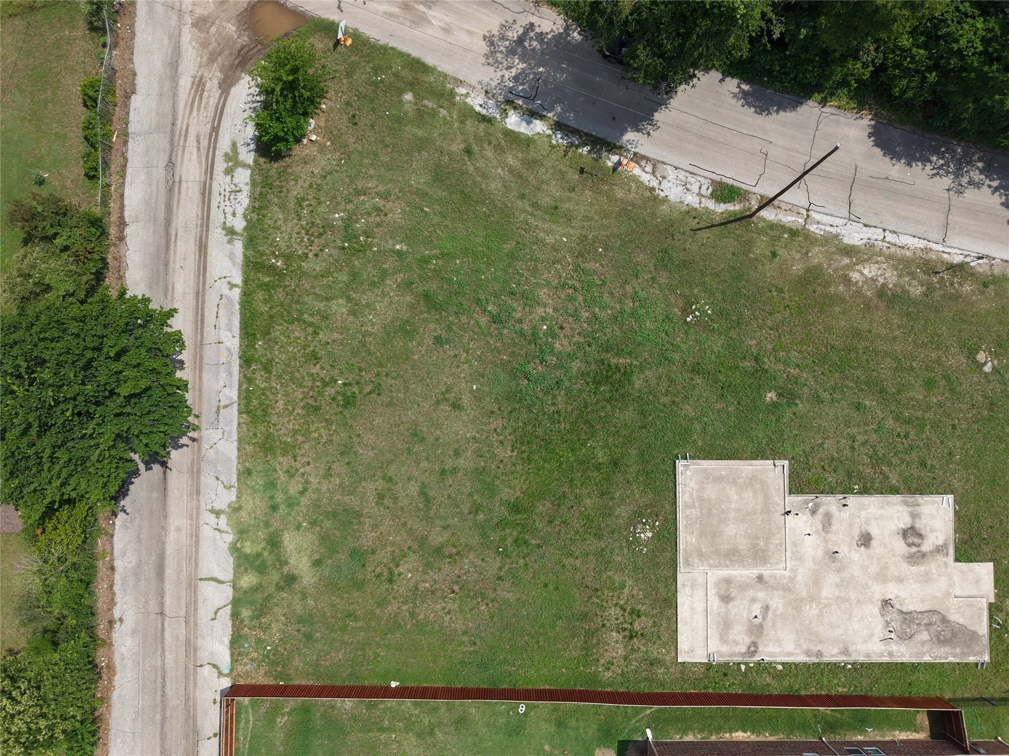 Expansive parcel featuring a concrete foundation, a partial perimeter fence, mature trees, and a grassy area