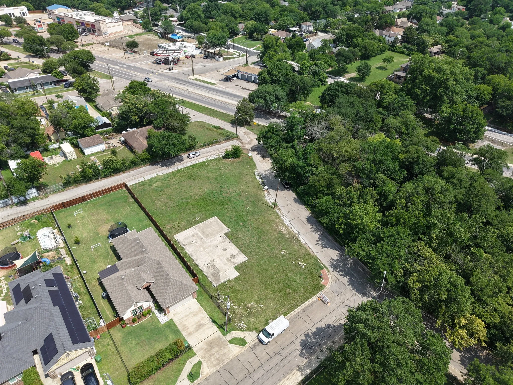 Expansive corner lot with existing concrete pad, bordered by established trees and a paved street