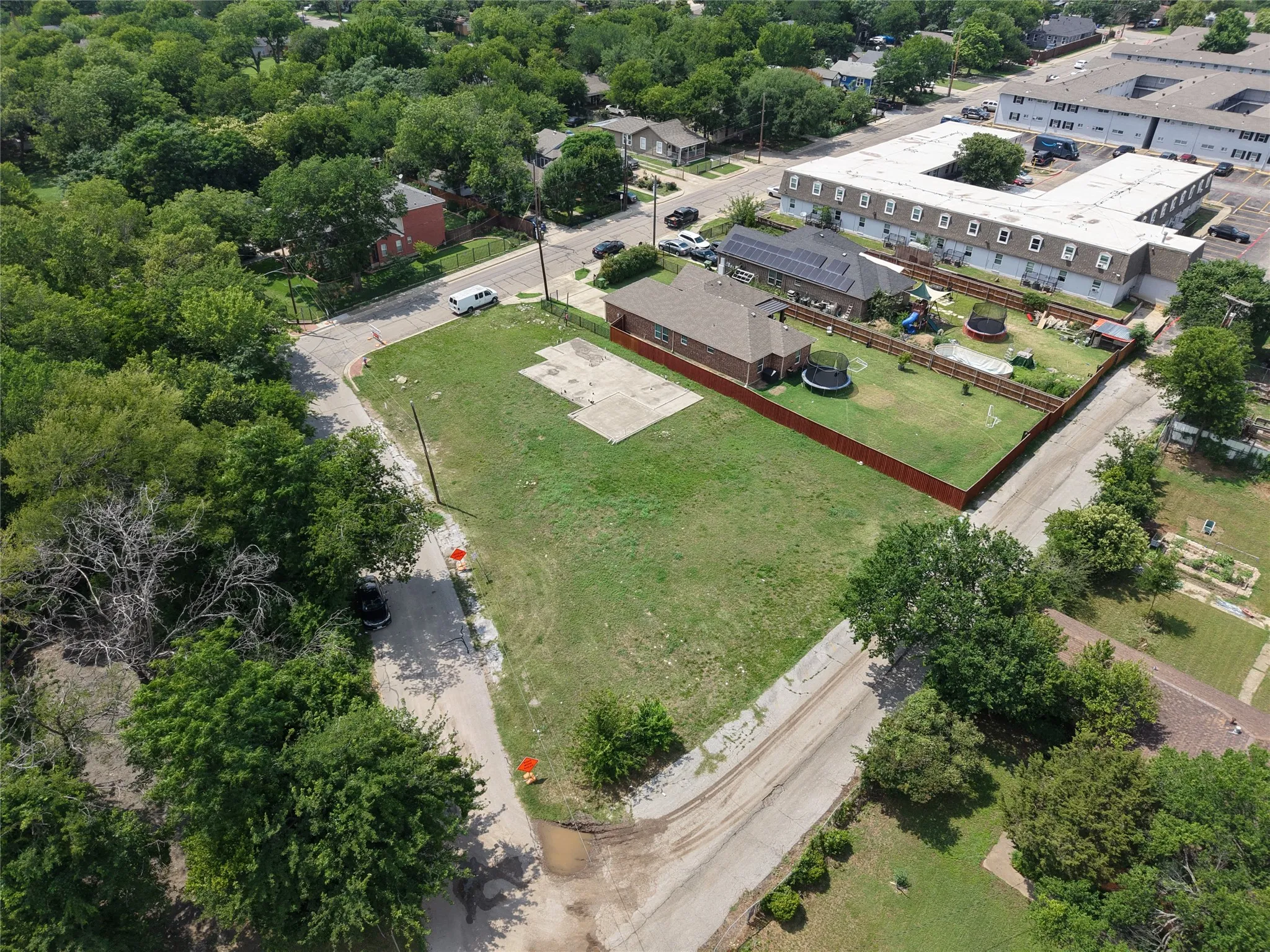 Expansive corner lot featuring a partial concrete slab, mature perimeter trees, and street frontage