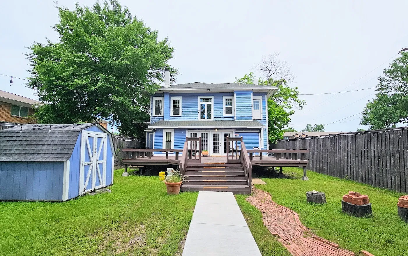 Rear exterior featuring a multi-level wood deck with stairs, a blue-painted storage shed, and a privacy fence