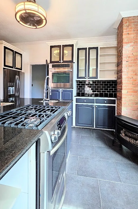 Contemporary kitchen featuring dark cabinetry, stainless steel appliances, and a black subway tile backsplash