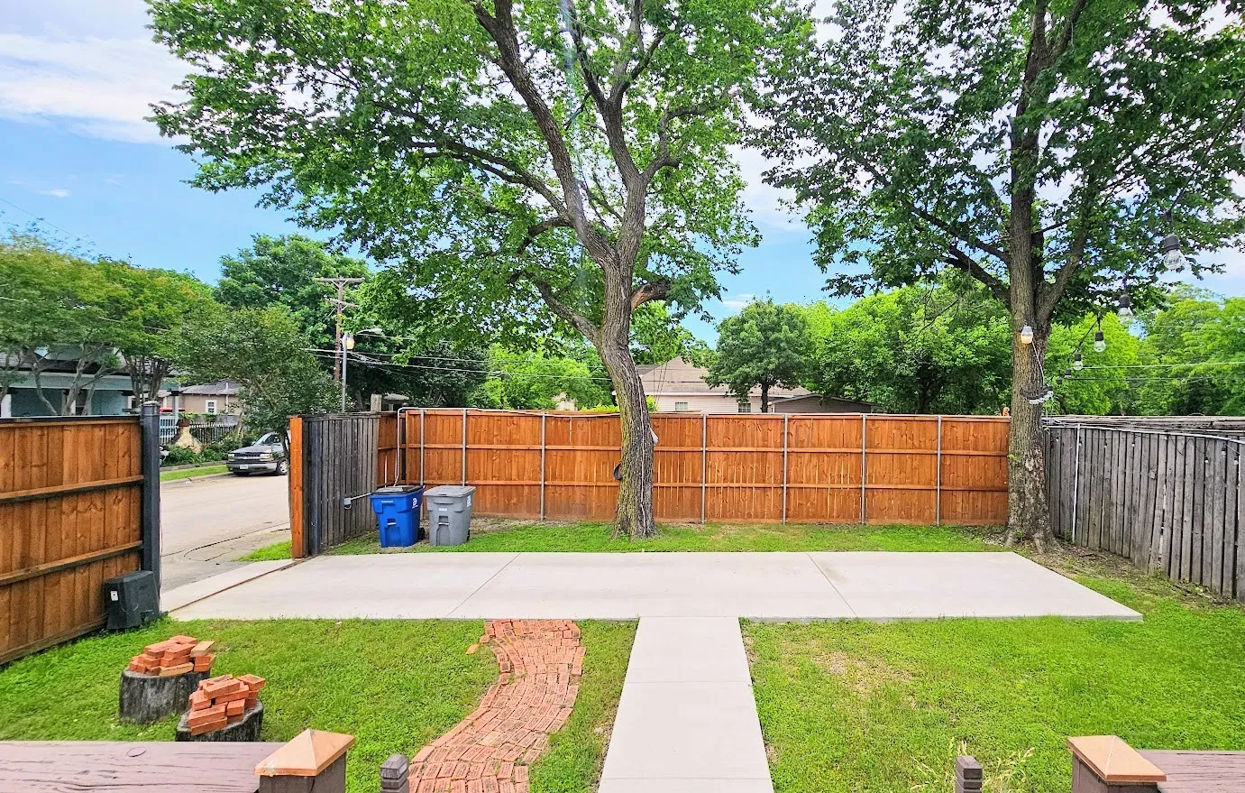 Expansive backyard featuring a concrete patio, mature trees, a manicured lawn, and a privacy fence