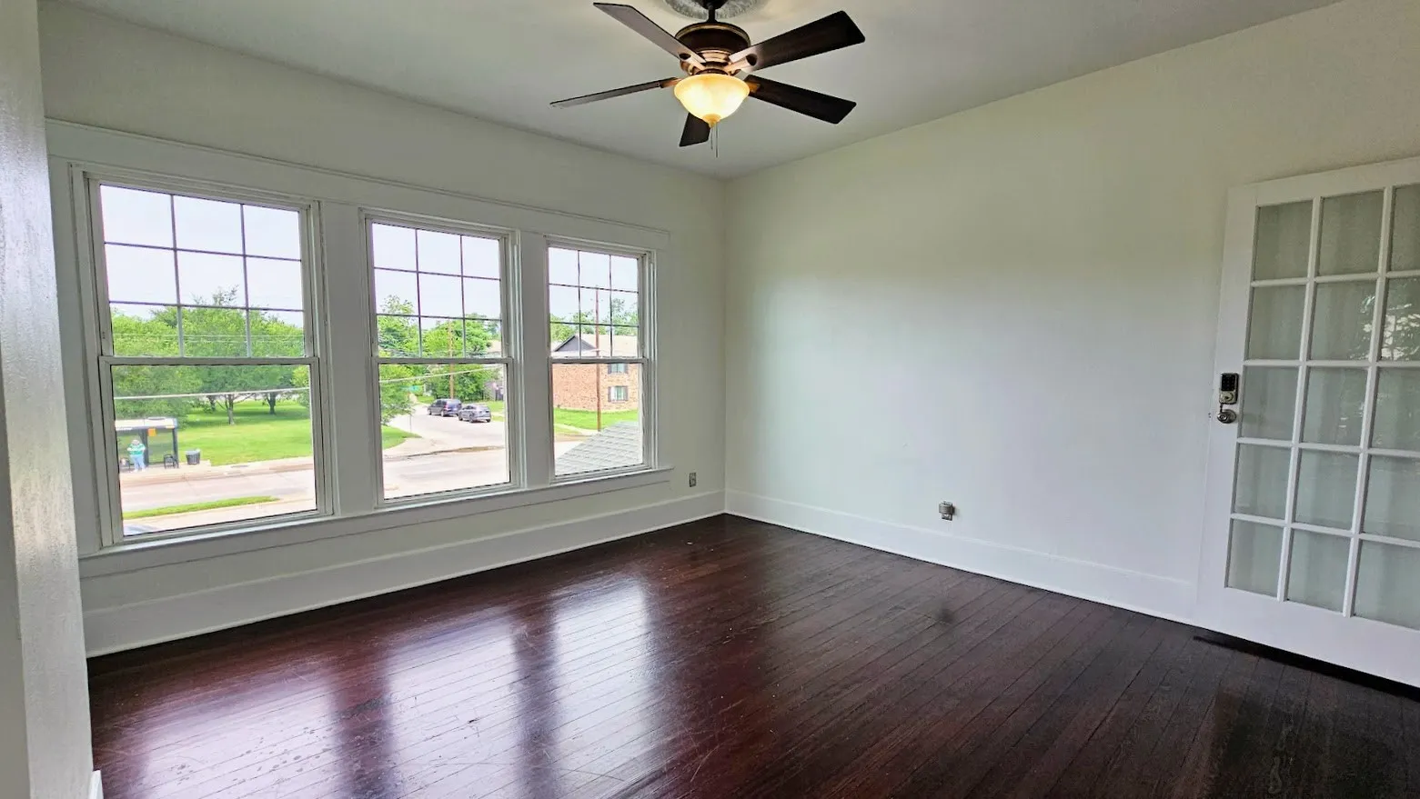 Room featuring a ceiling fan with integrated lighting, a french door with glass panels, a trio of large grid-pattern windows, wood-finish flooring, and white baseboards